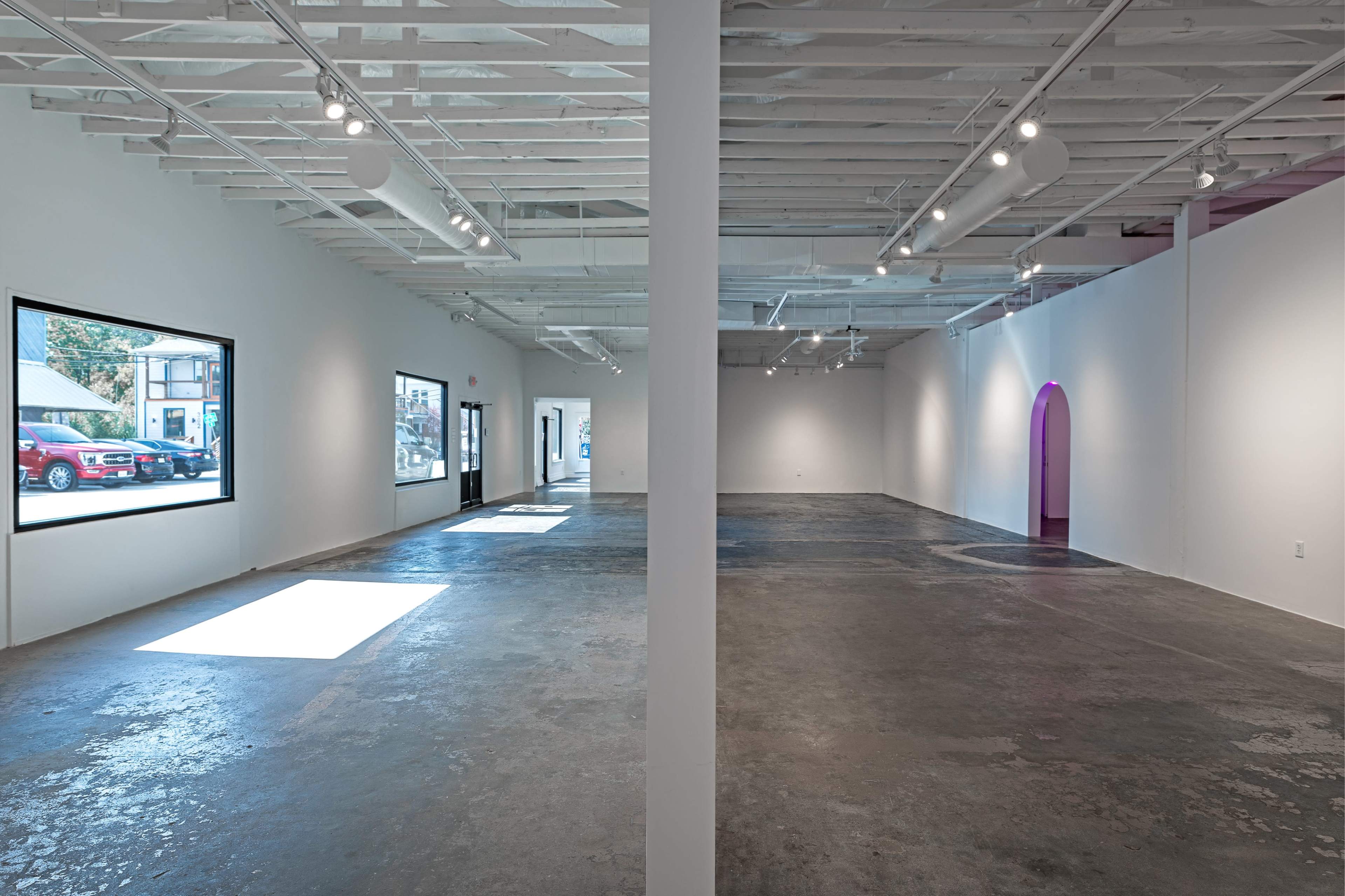 A spacious, empty art gallery with a polished concrete floor, exposed beams, and large windows allowing natural light to enter.