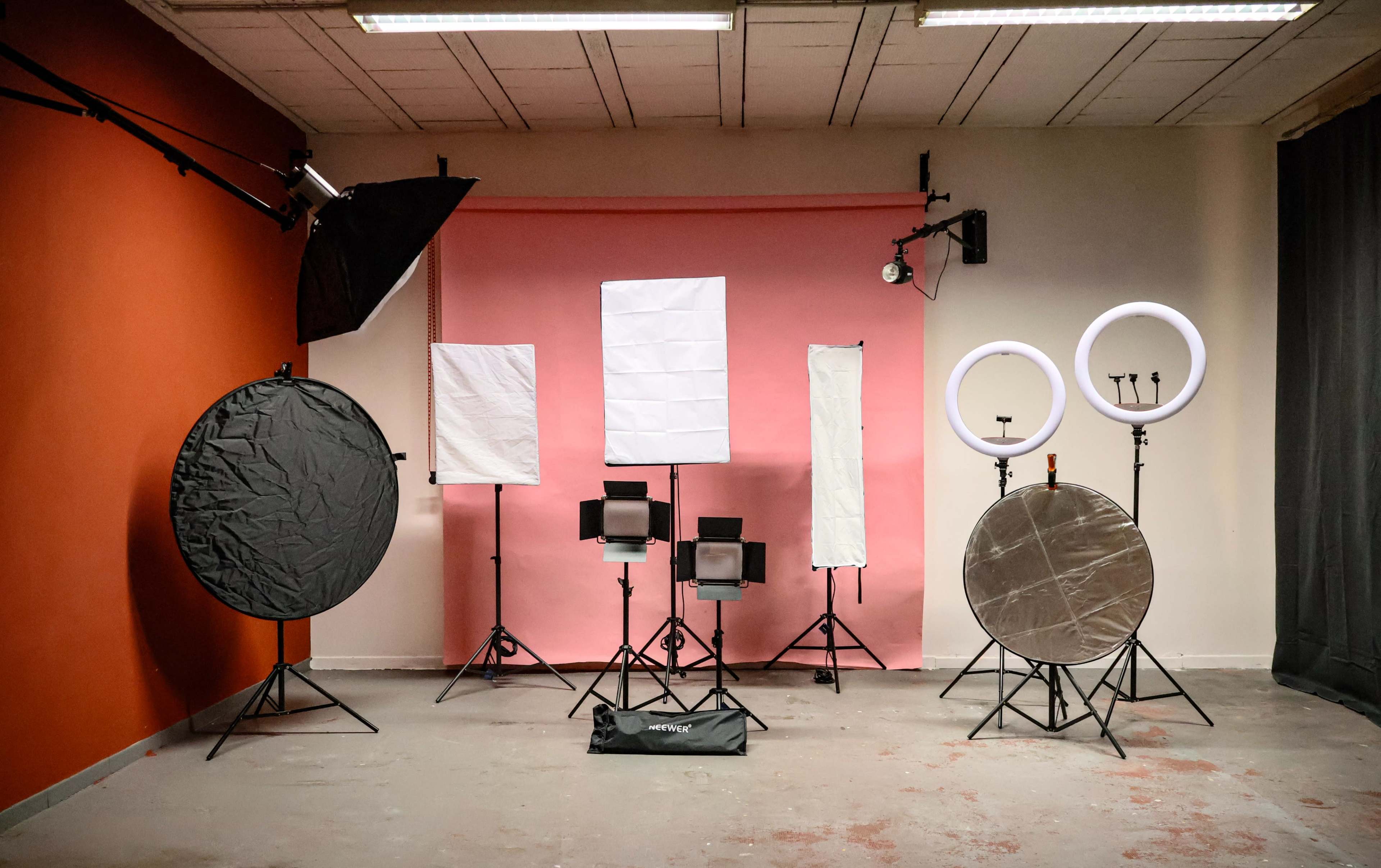 The image shows a photography studio setup with various lighting equipment and backdrops arranged against a colored wall.