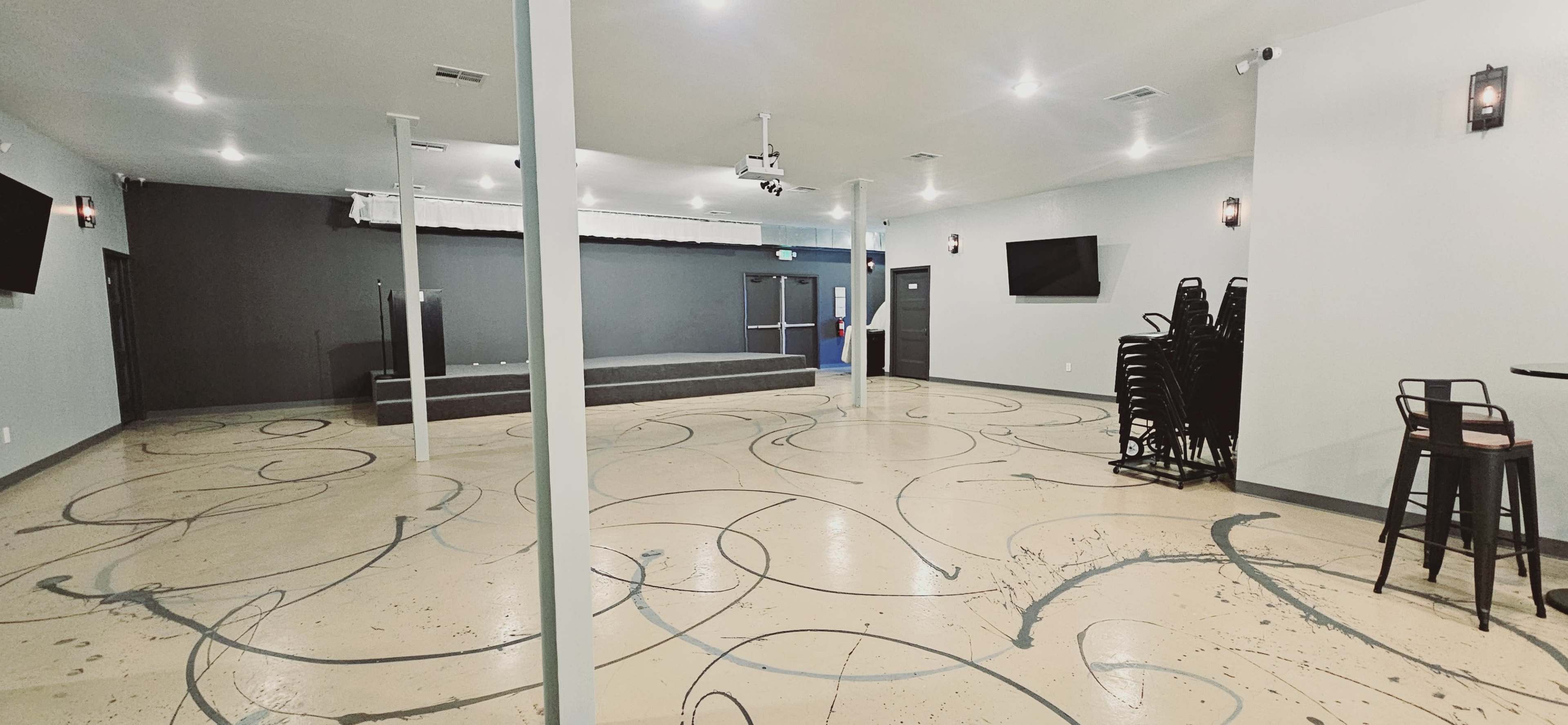 A spacious interior with a polished floor featuring swirling designs, a small stage at the back, and seating arrangements on the sides.