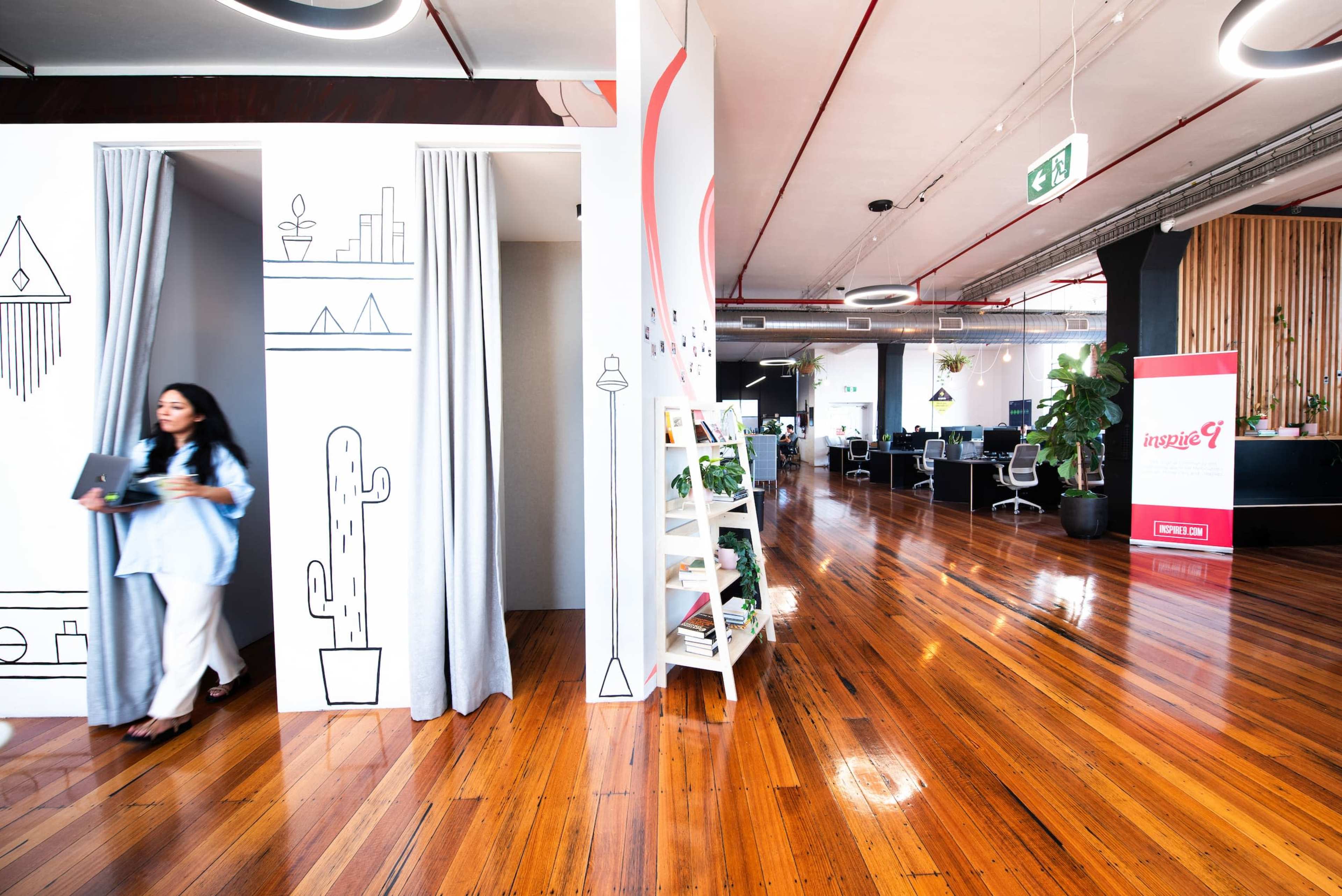A woman exits a cubicle area in a modern office with wooden floors and contemporary design elements.