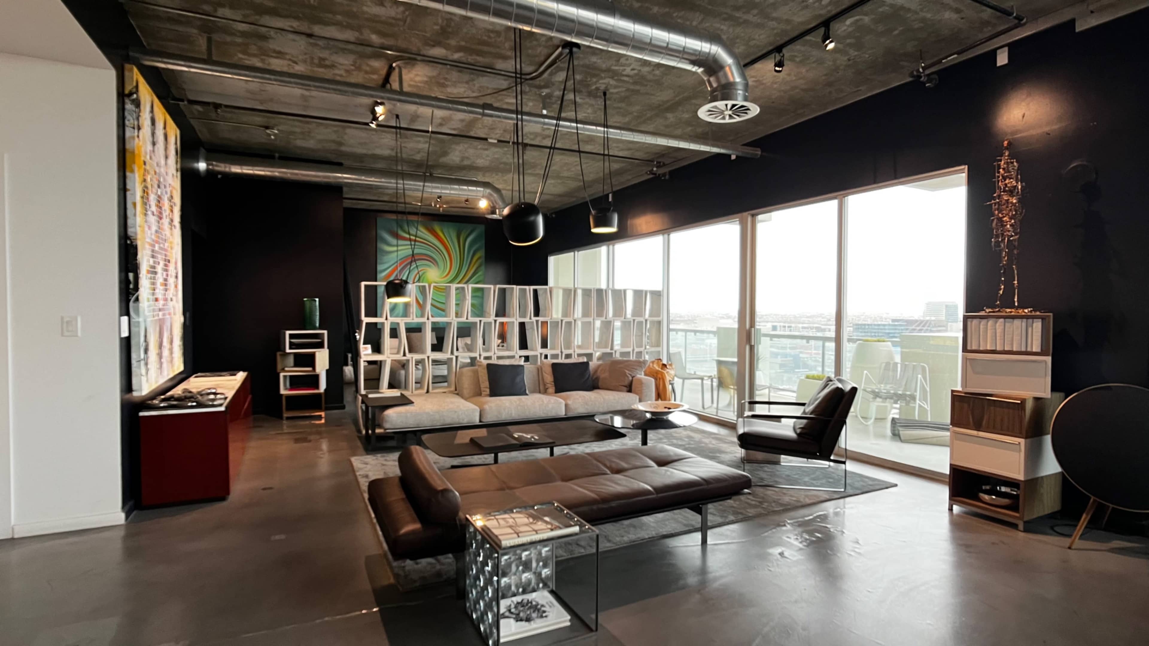 A modern living room with a sectional sofa, sleek furniture, large windows, and an abstract mural on the wall.