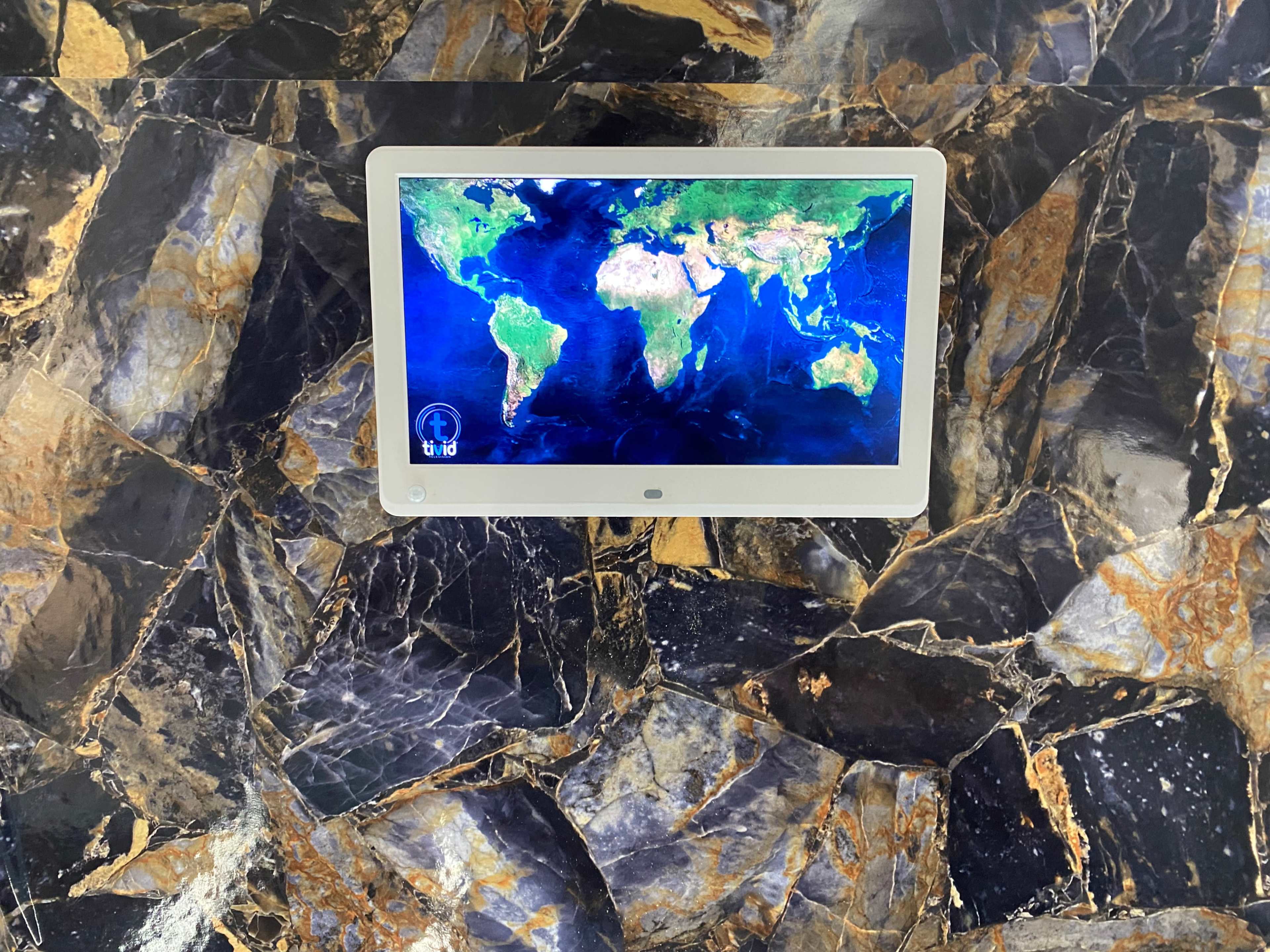 A digital display showing a map of the world is mounted on a wall with a textured, dark stone surface.