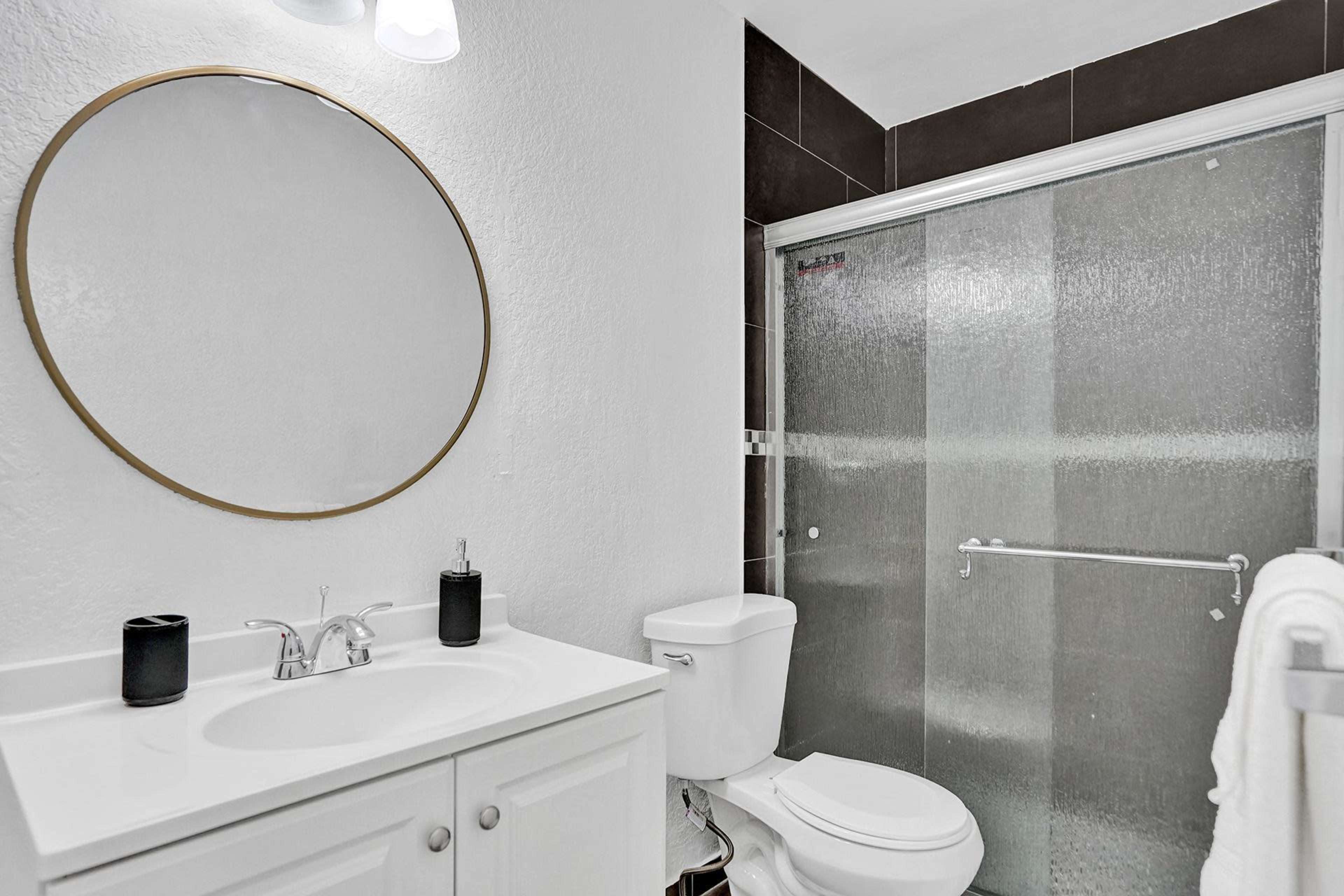 A modern bathroom with a circular mirror above a white sink and a glass-enclosed shower.