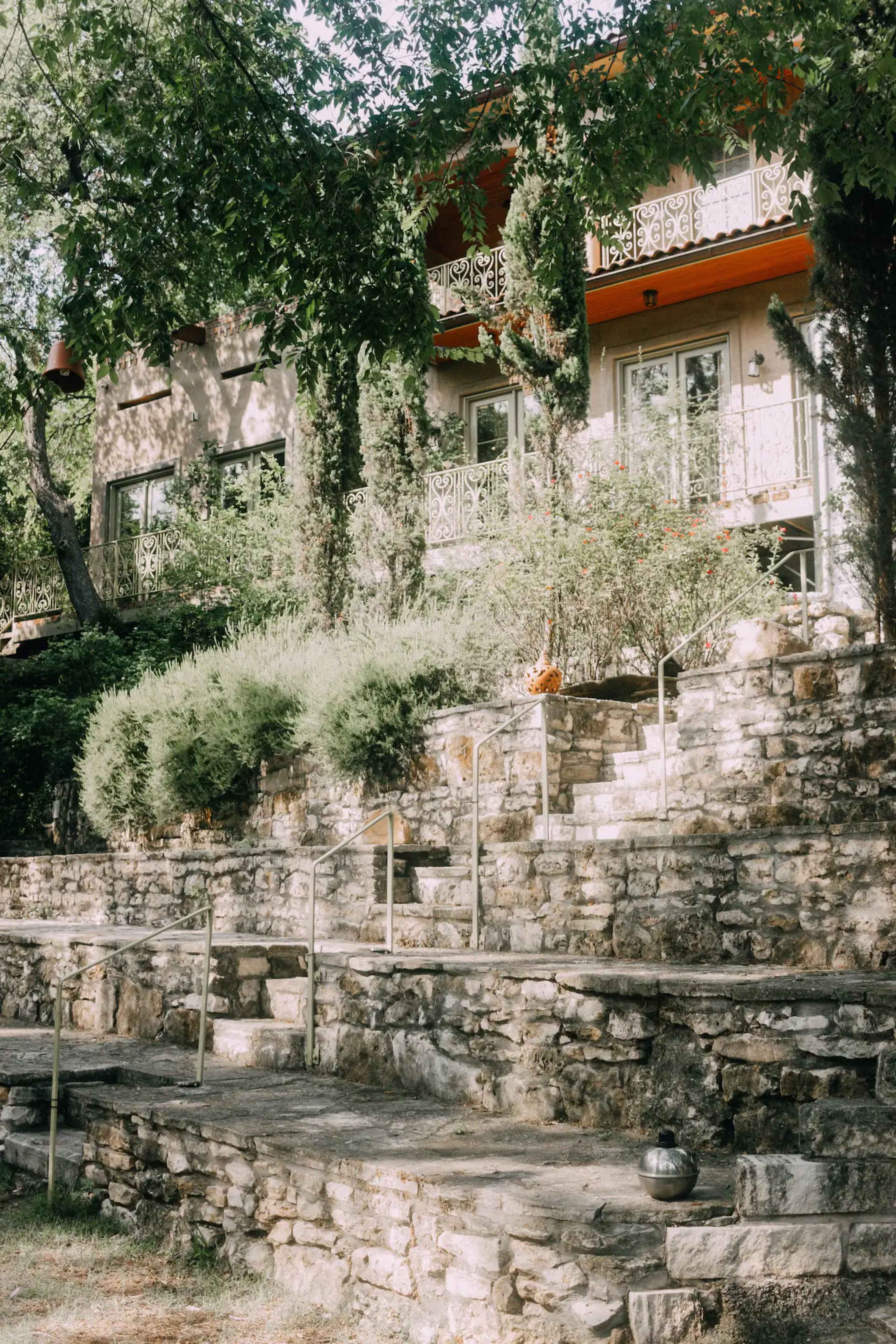 A stone staircase leads up to a two-story house surrounded by trees and shrubs.