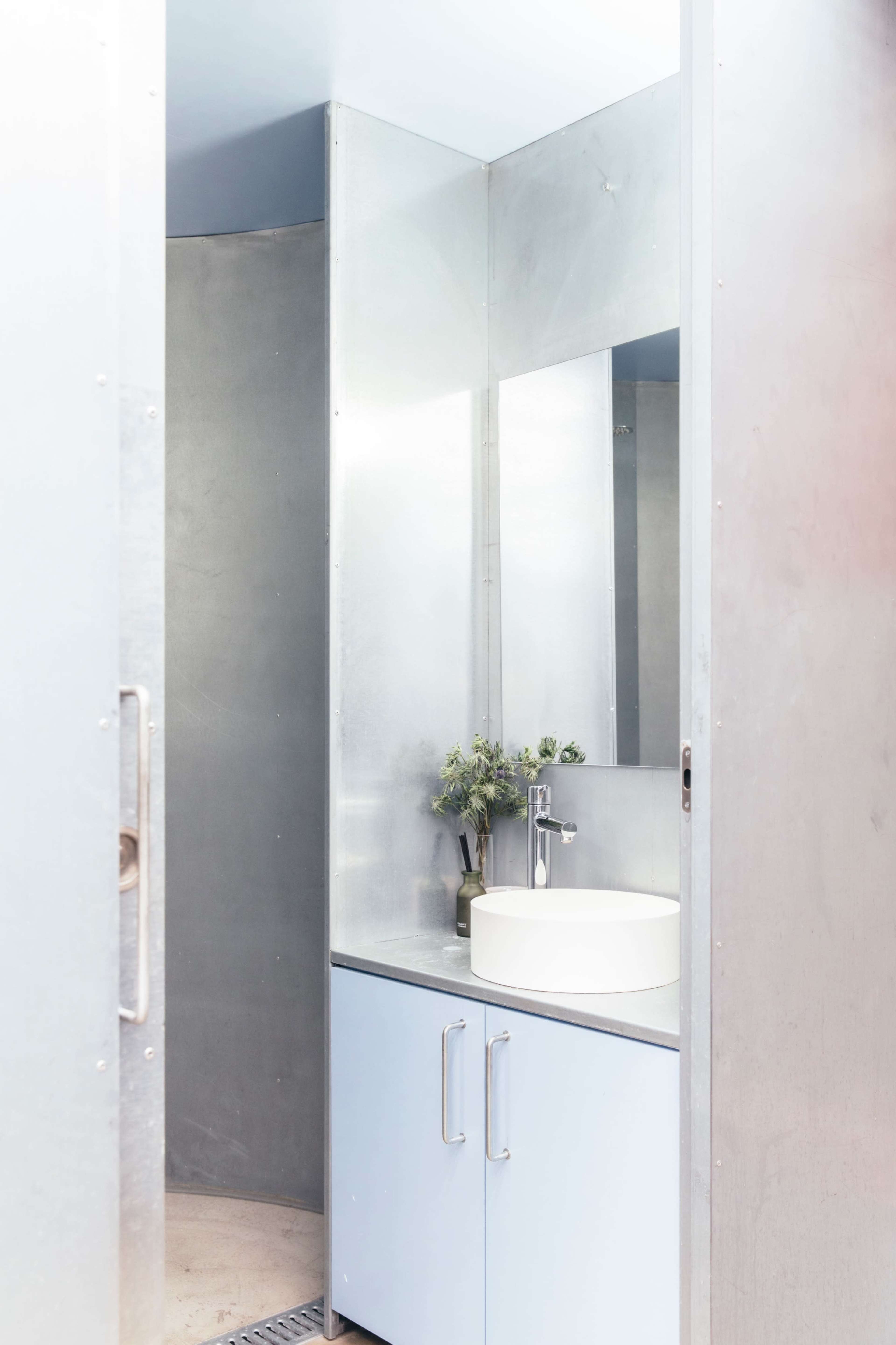 The image shows a modern bathroom with a circular design, featuring a white sink, a large mirror, and light blue cabinetry.