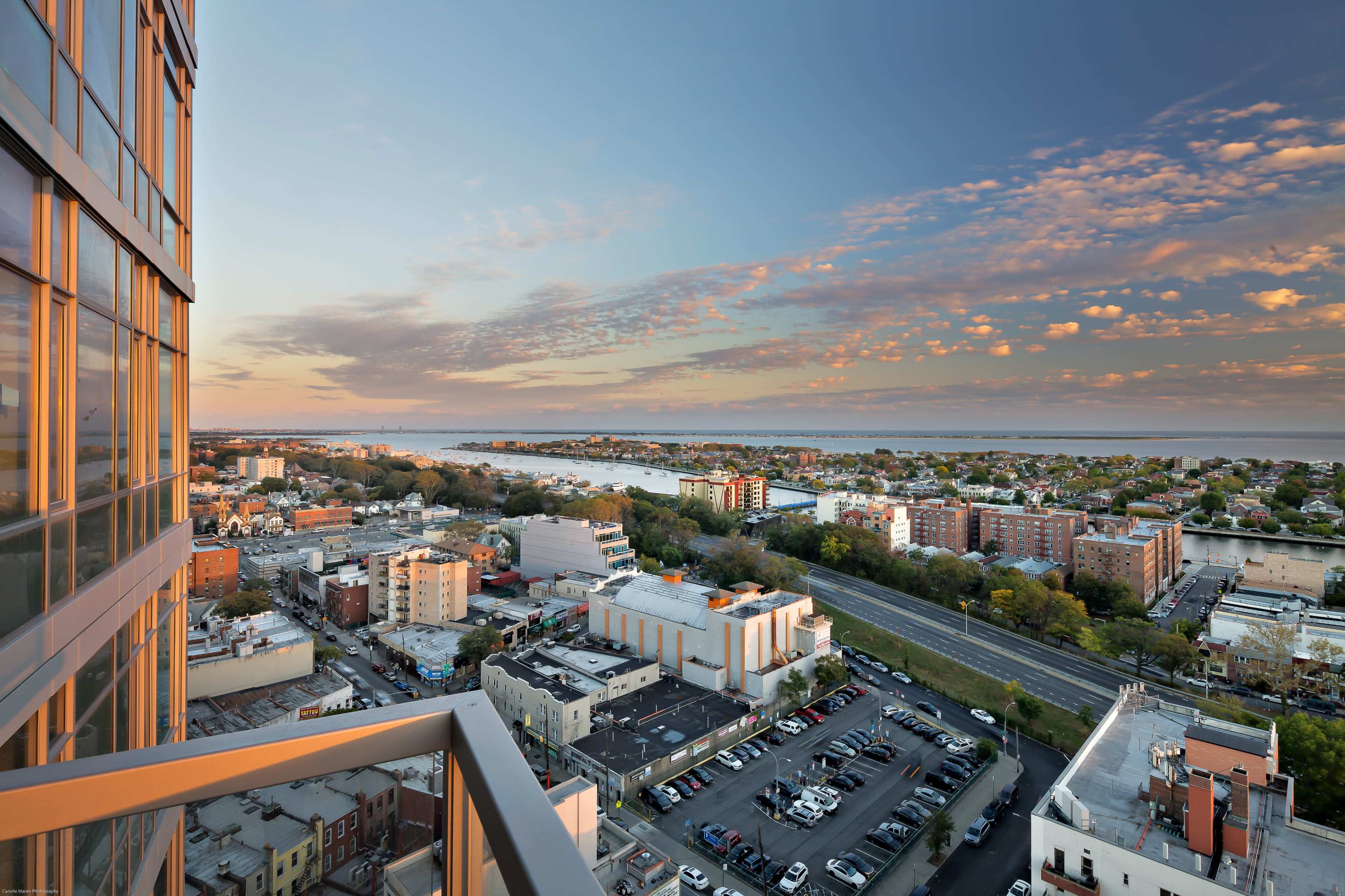 A panoramic view of a cityscape from a high-rise building, overlooking residential areas and a waterfront at sunset.