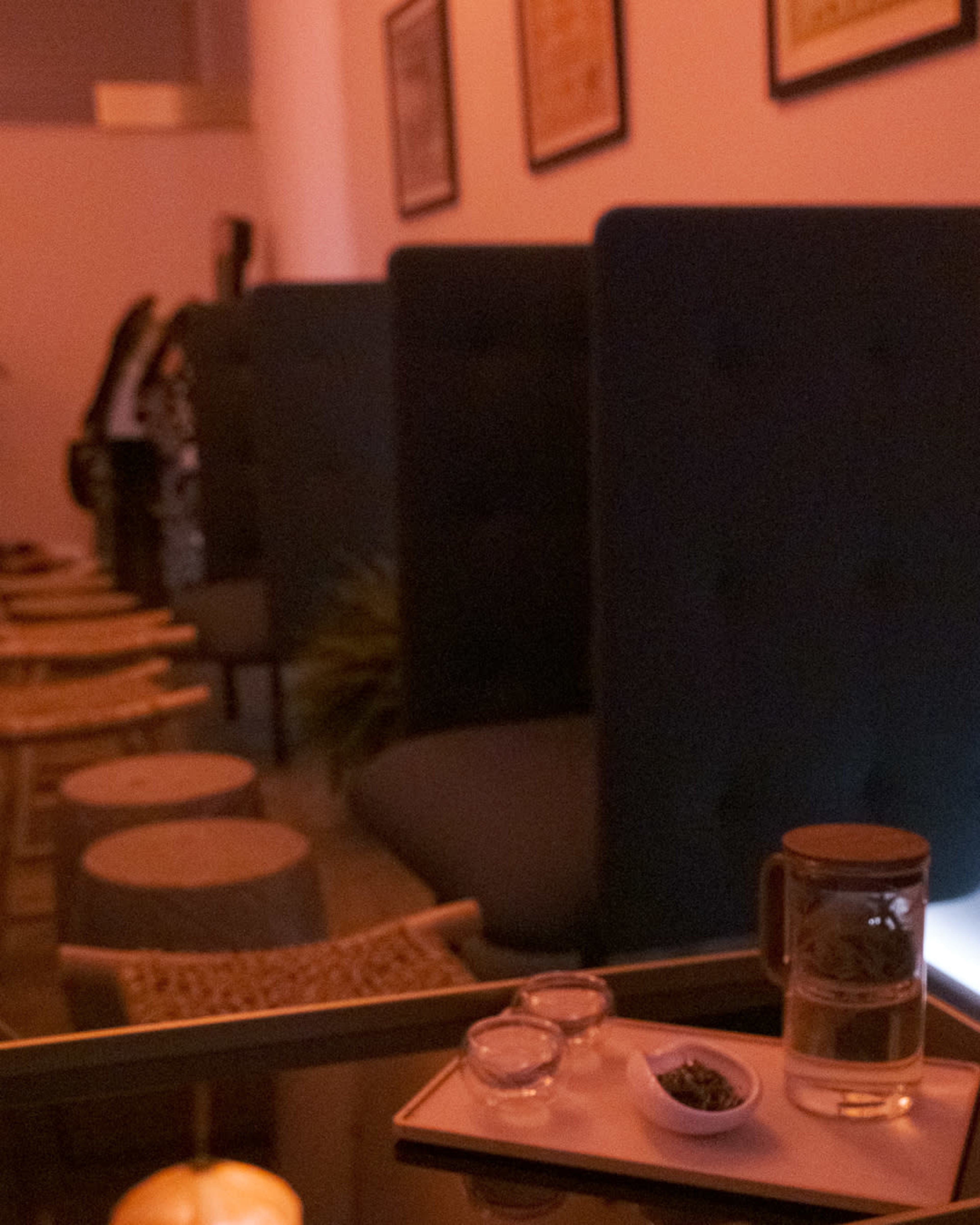 The image shows a dimly lit cafe with empty tables and a glass of water on a table, accompanied by small plates.