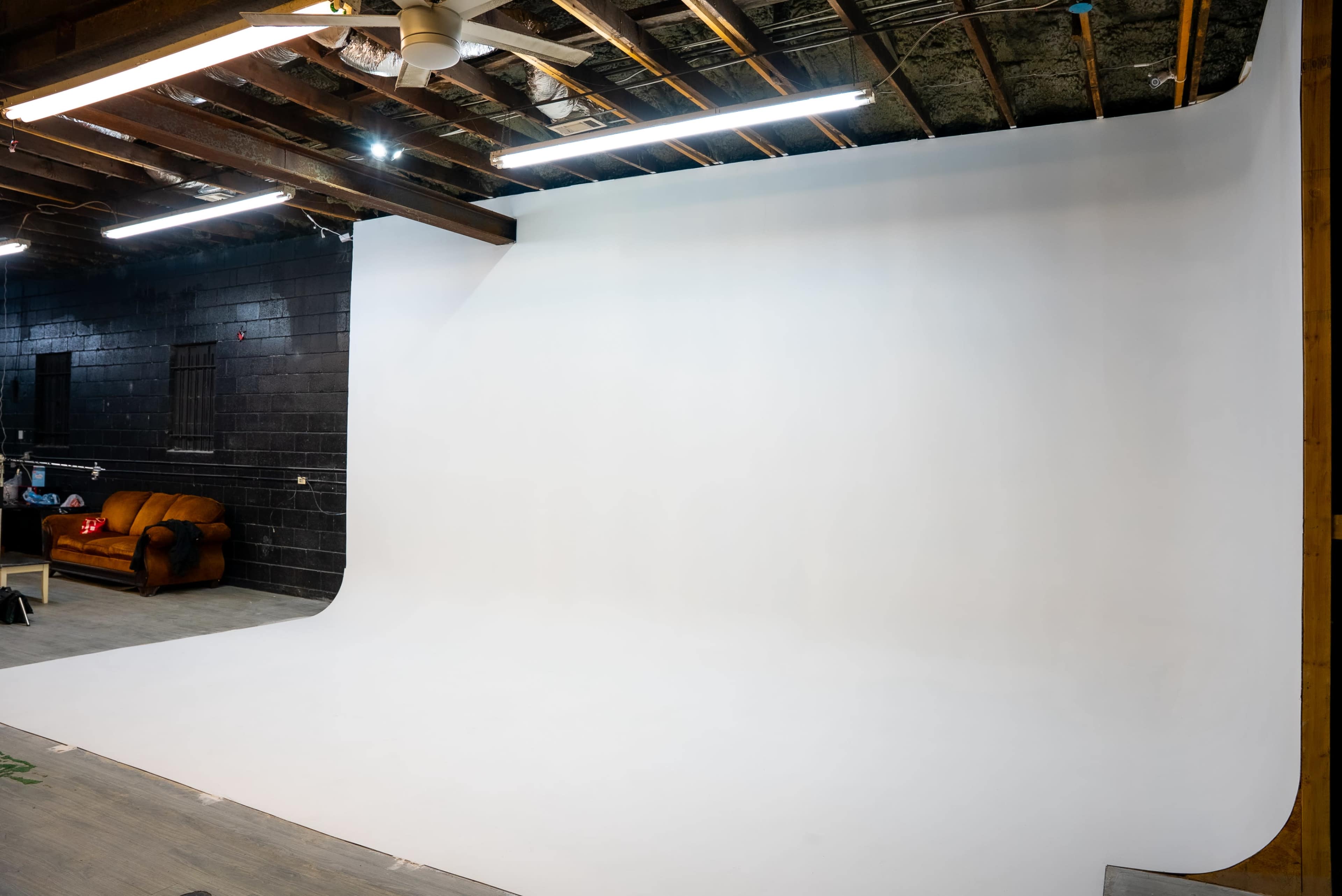 The image shows a photography studio with a large white backdrop and a brown sofa placed against one wall.