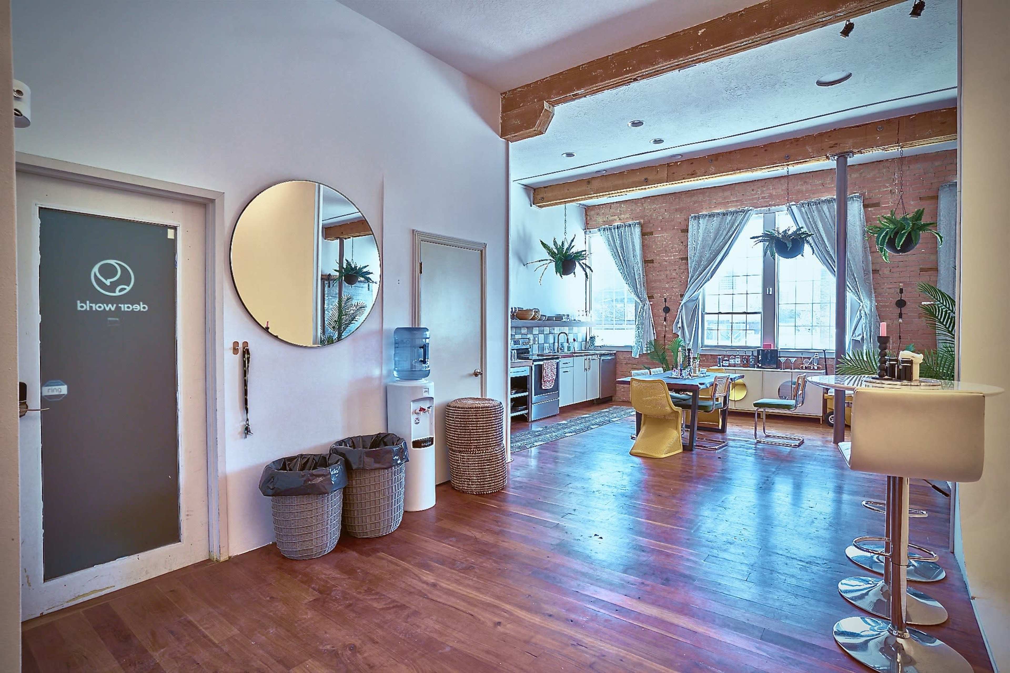 A spacious, well-lit interior featuring a kitchen area, a circular mirror, and plants hanging from the ceiling.