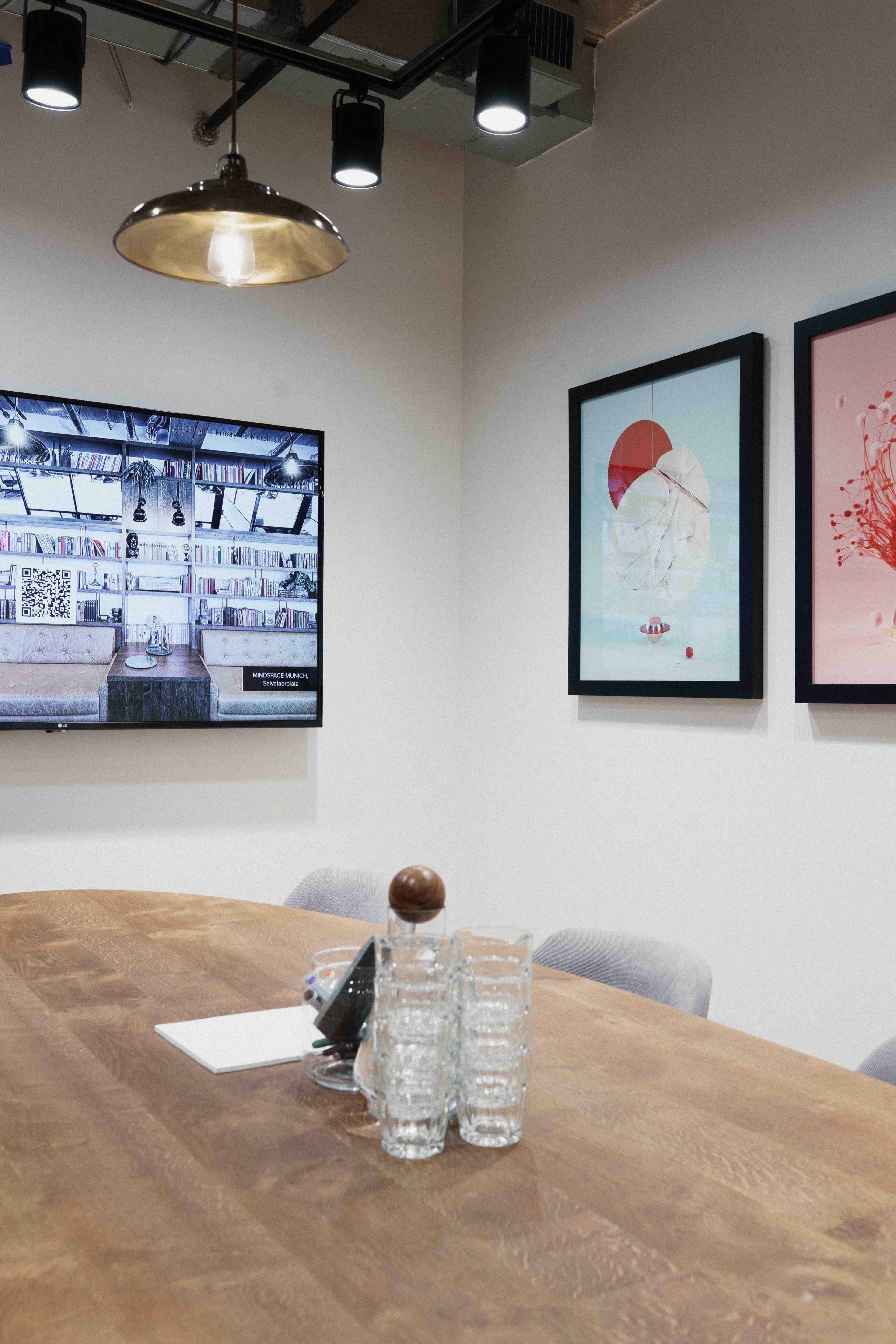 A modern conference room features a wooden table, a television mounted on the wall, and two framed artworks.