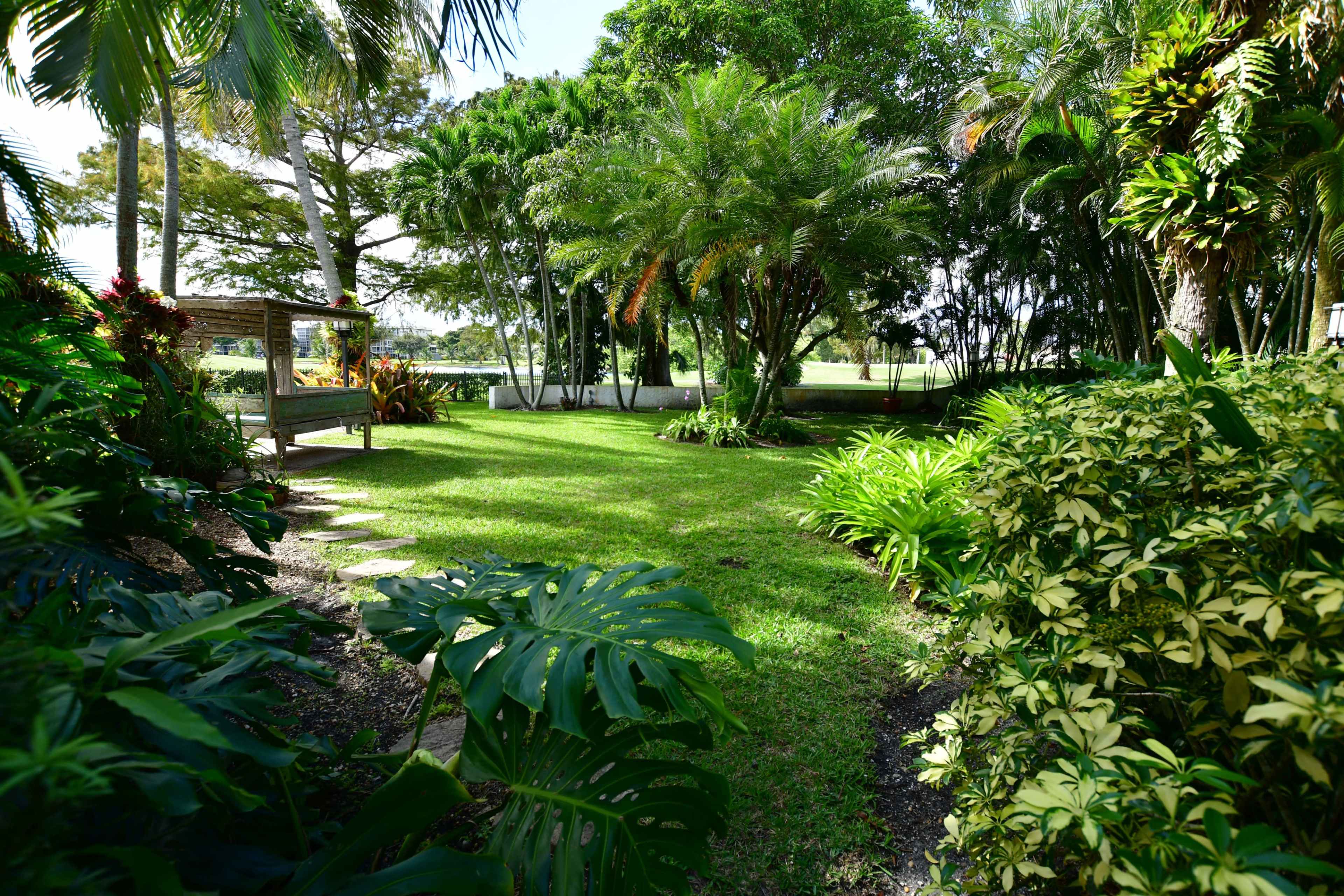 The image shows a well-maintained garden with lush greenery, stone pathways, and tropical plants.