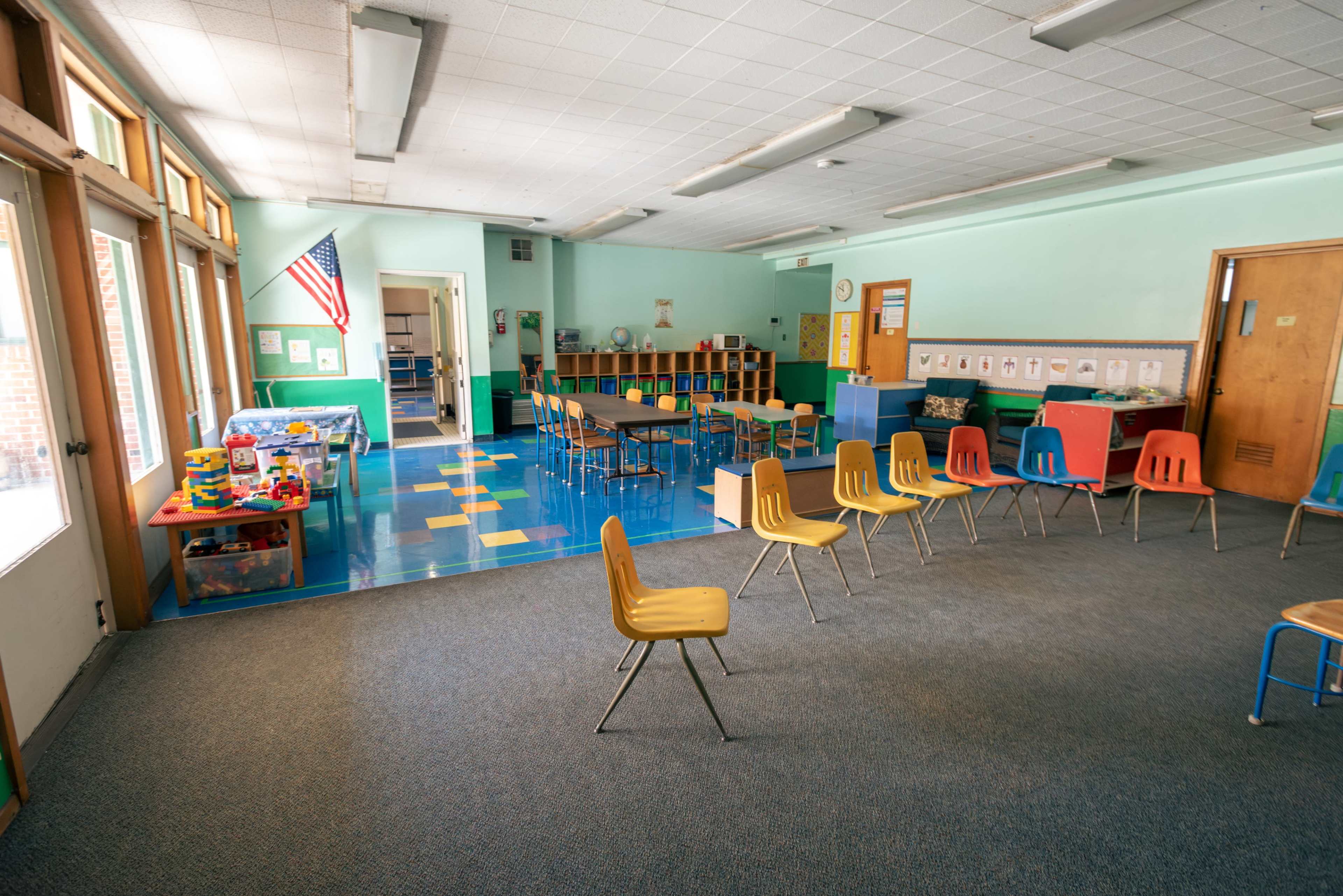 A classroom is laid out with colorful chairs and tables, featuring a read area and play area equipped with toys.