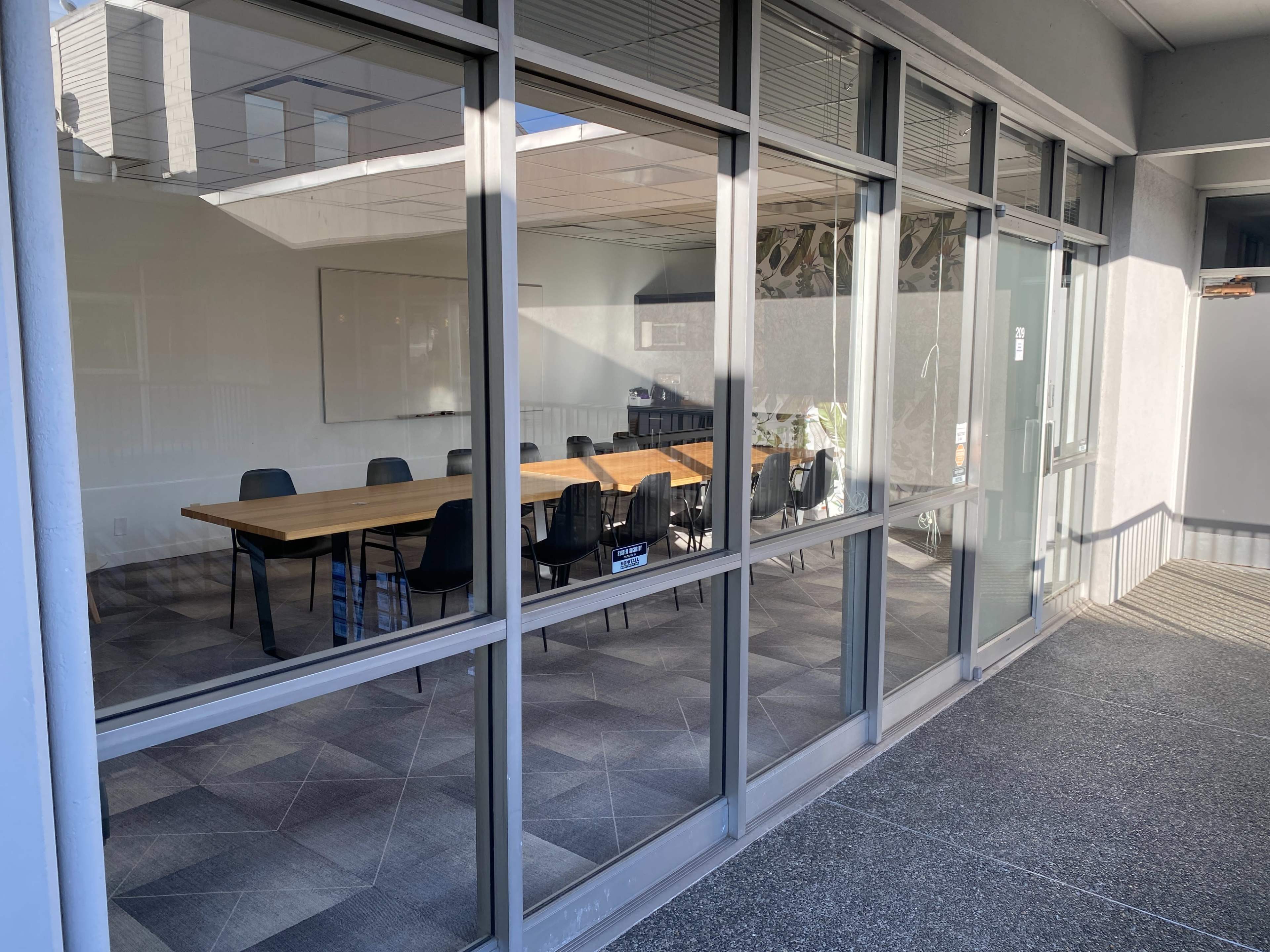 A conference room with a long wooden table and several black chairs is visible through large glass windows.