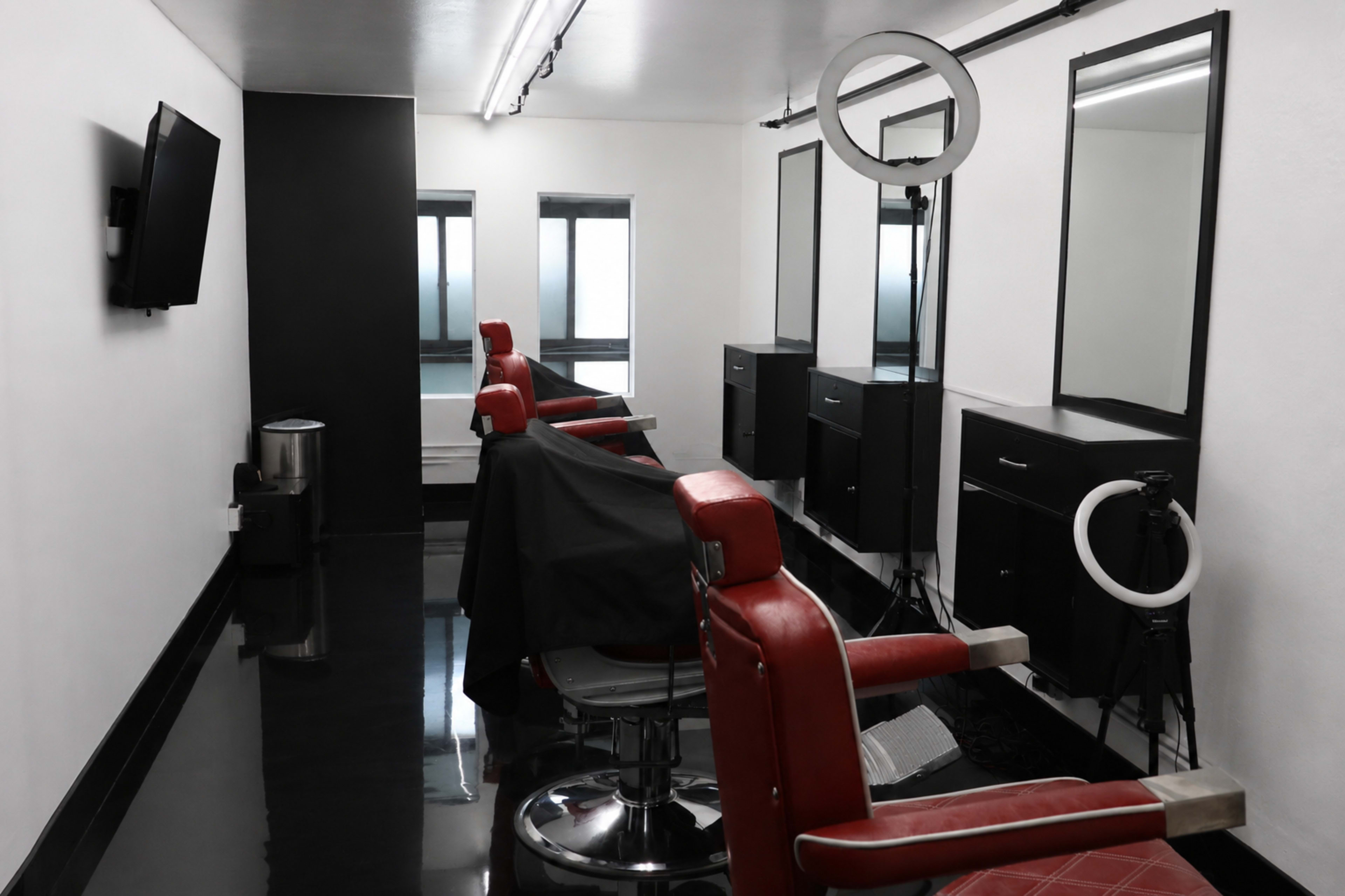 The image shows a modern barber shop interior featuring red barber chairs, large mirrors, black cabinetry, and a sleek black floor.