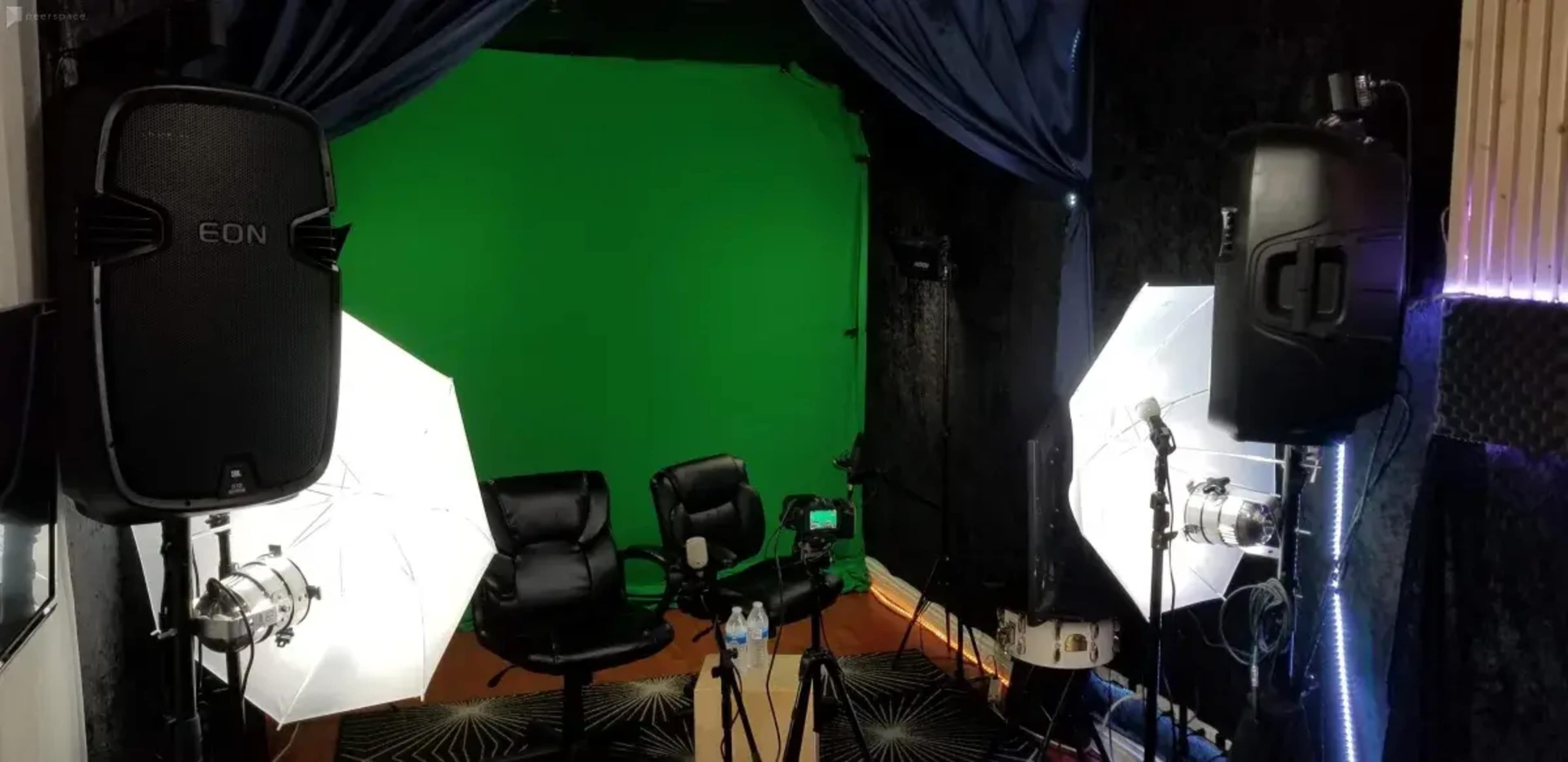 The image shows a video production setup featuring two black chairs in front of a green screen, surrounded by lighting equipment and a camera on a tripod.