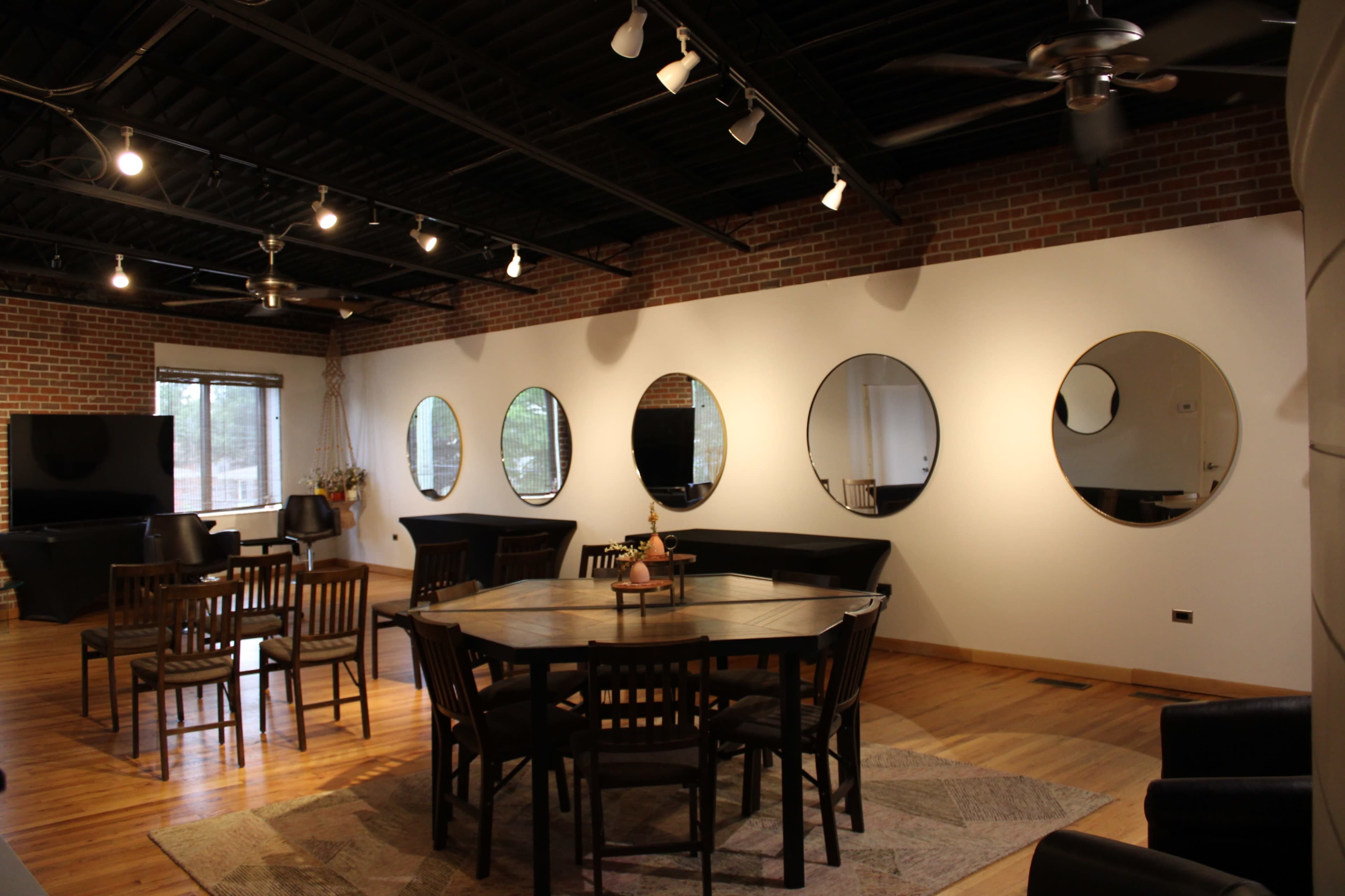 A modern interior space with a wooden dining table and chairs, a large television on one side, and several round mirrors mounted on a white wall.