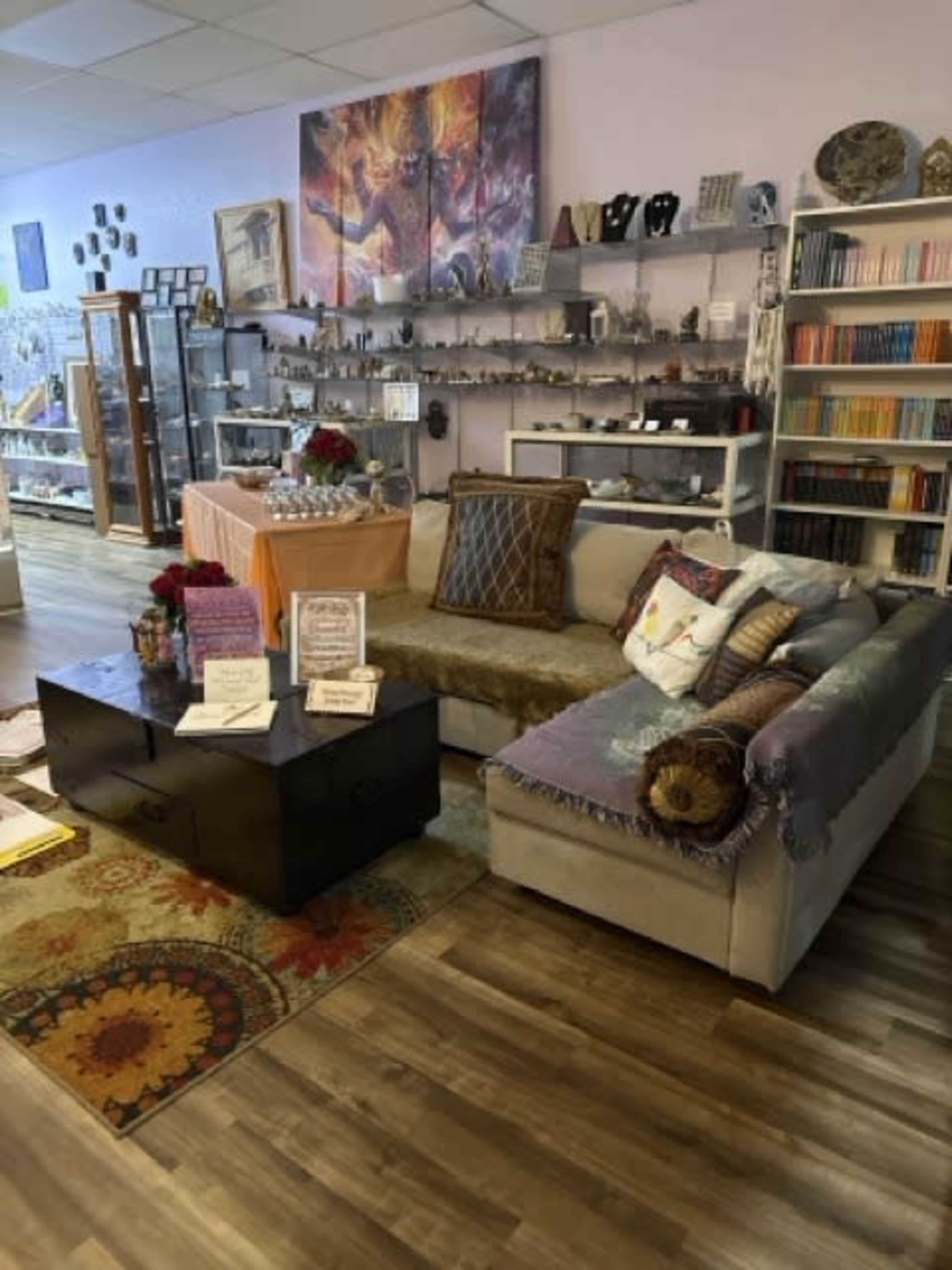 The image shows a cozy retail space featuring a seating area with a sectional sofa, a coffee table, and shelves lined with various decorative items and books.