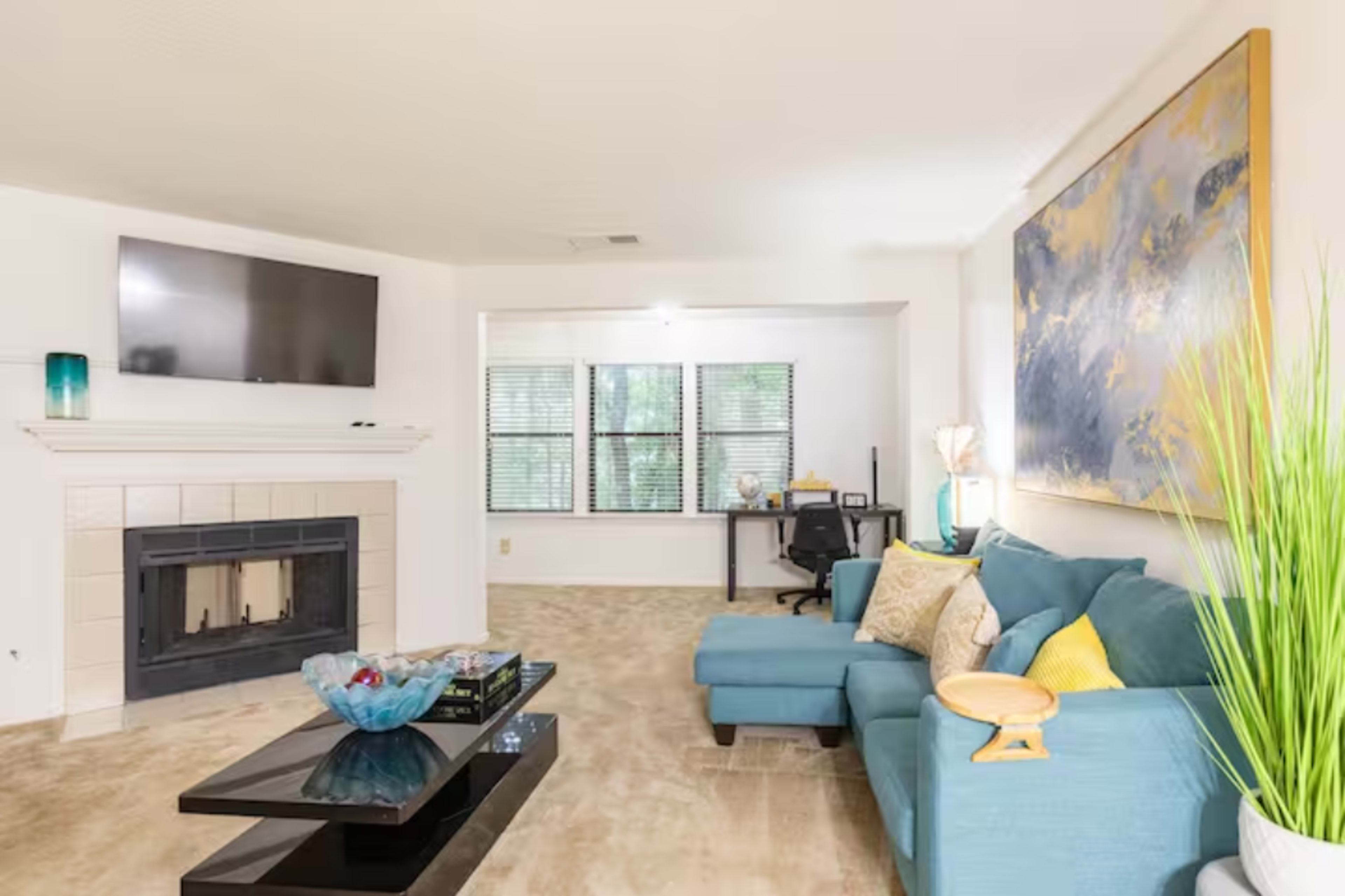 A living room with a turquoise couch, a black coffee table, a fireplace, and a wall-mounted TV.