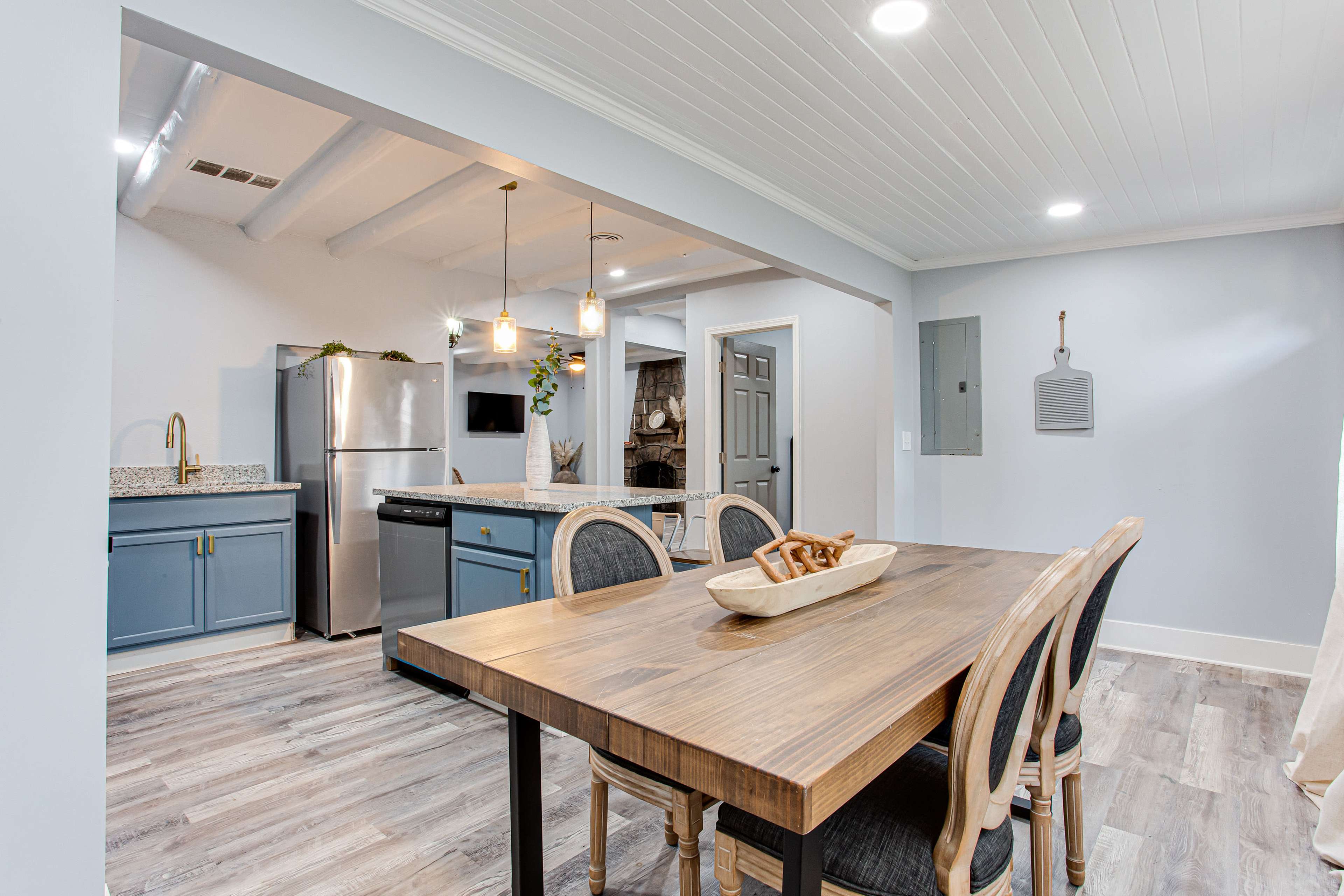 A modern kitchen and dining area featuring a wooden dining table, blue cabinetry, stainless steel appliances, and a light, airy decor.