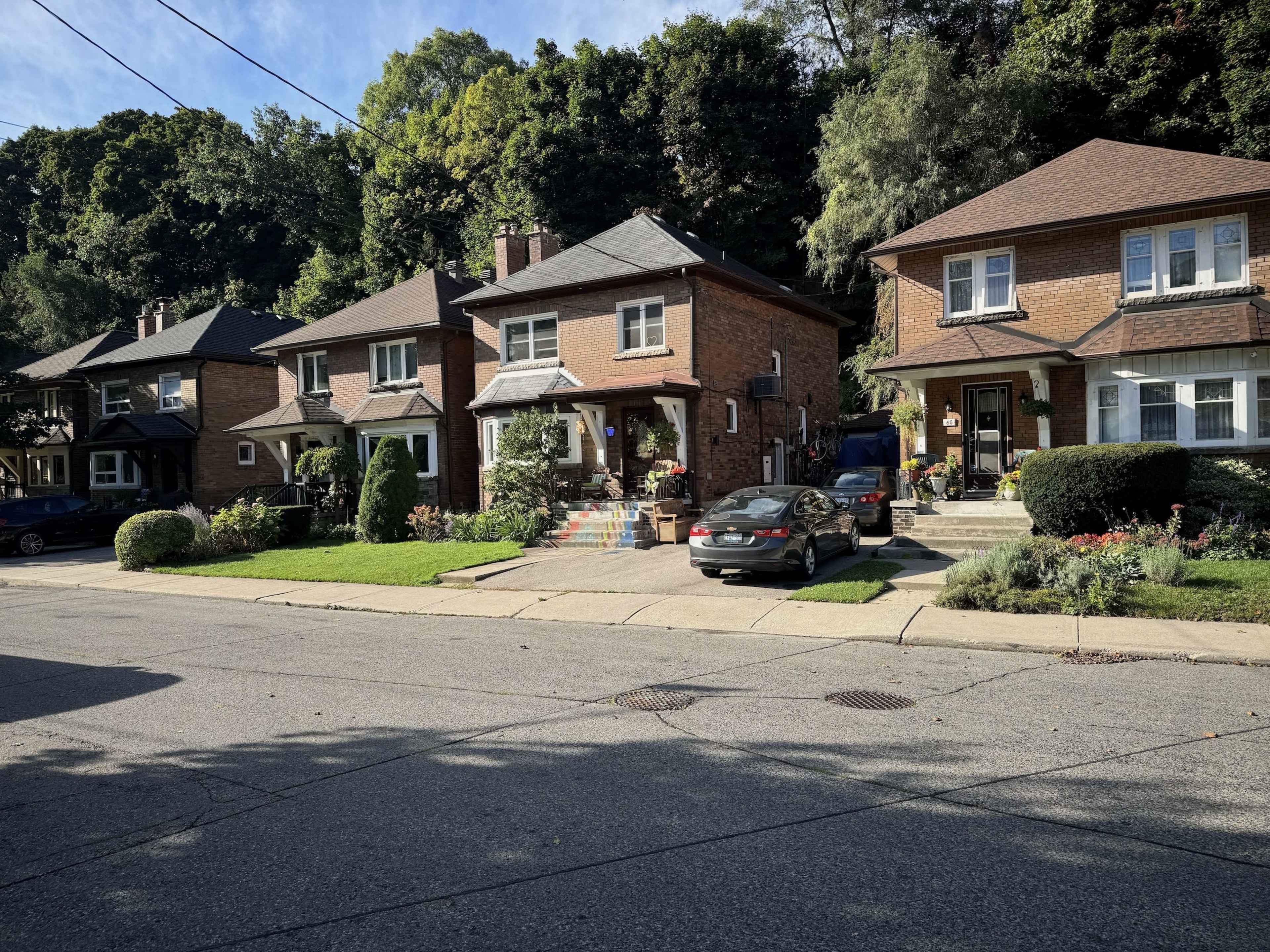 The image shows a row of three residential homes with well-maintained gardens on a tree-lined street.