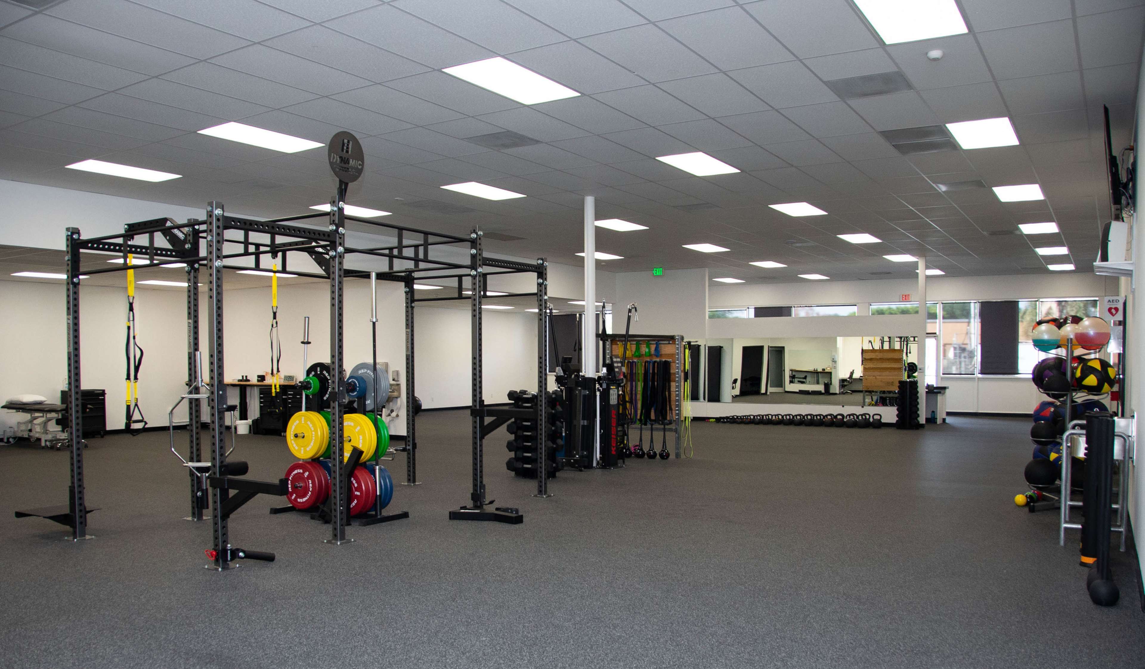 A well-equipped gym featuring a weightlifting rack, various weights, and exercise equipment in a spacious, brightly lit area.