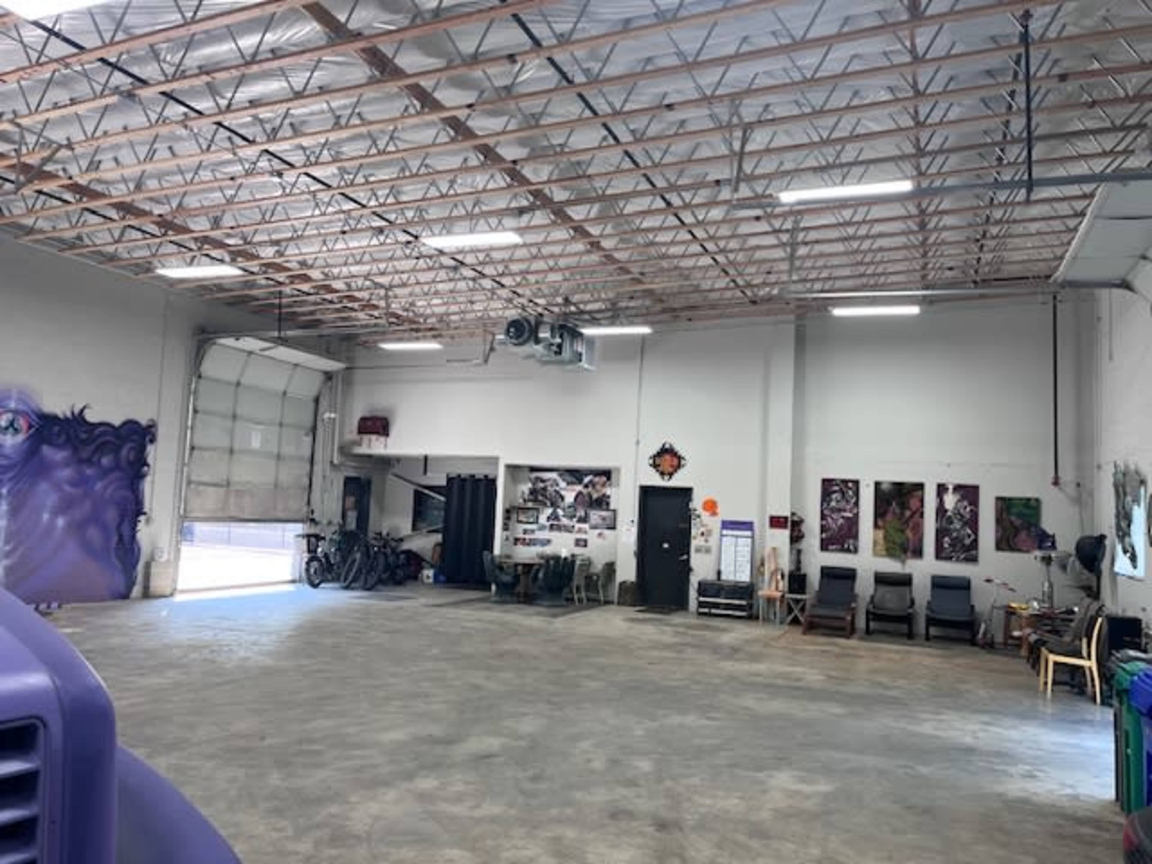 A spacious garage with concrete flooring, open doors, and various items such as bicycles and chairs along the walls.