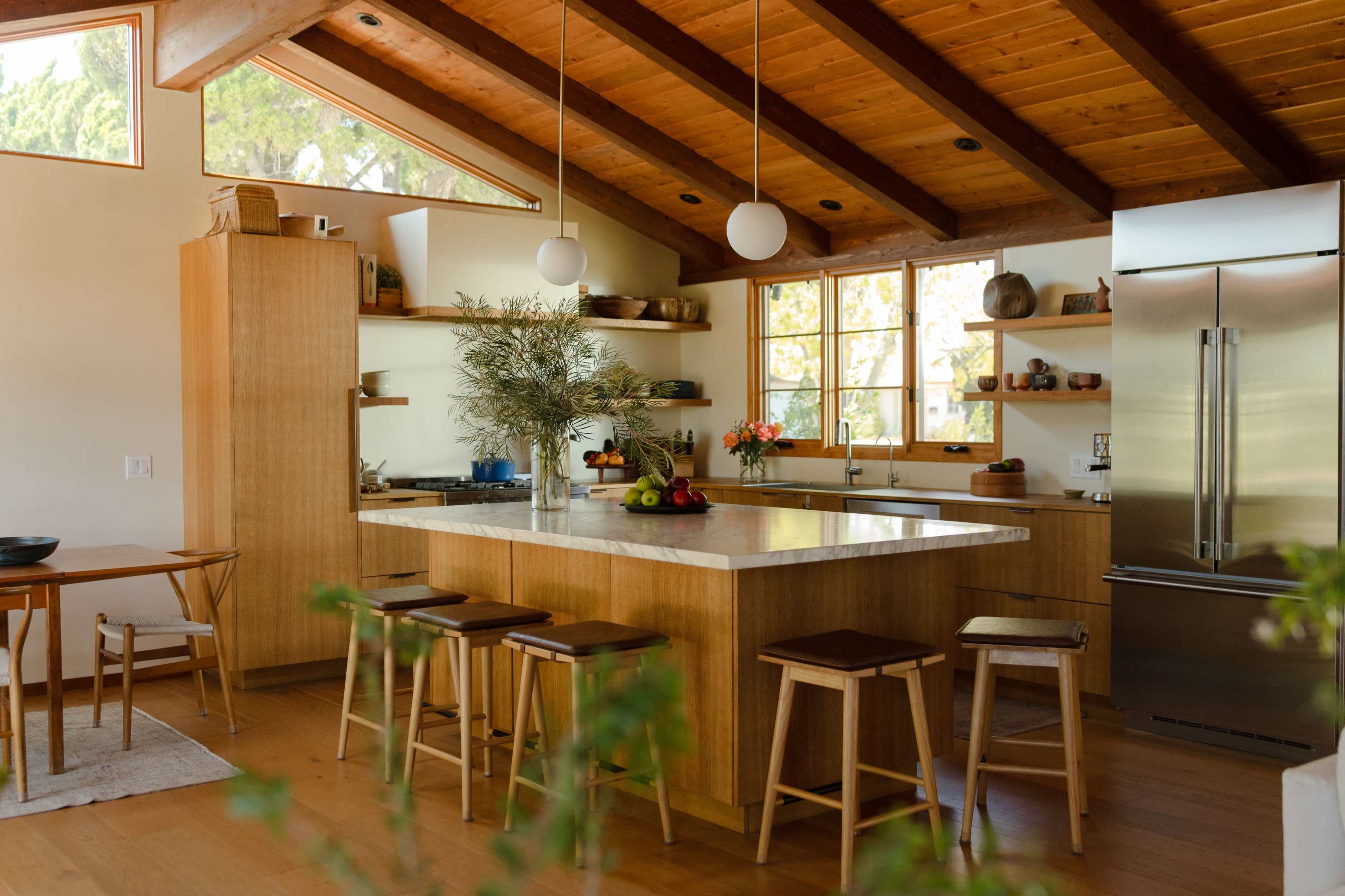 A modern kitchen features wooden cabinetry, a large island with a marble countertop, and a variety of kitchen appliances.