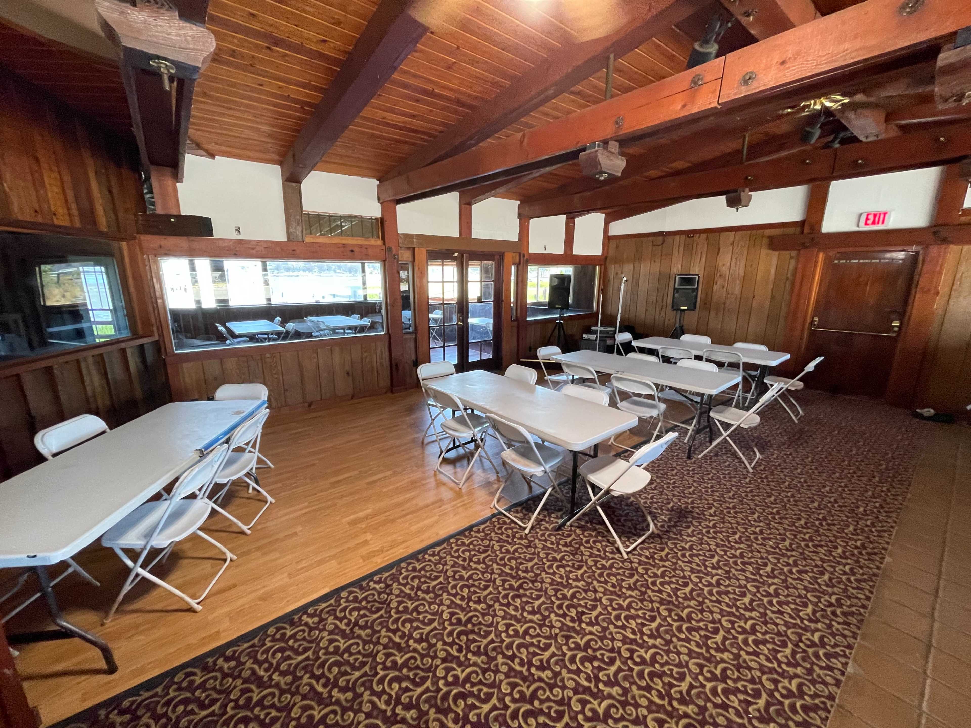 A spacious wooden-paneled interior room set up with multiple folding tables and chairs.