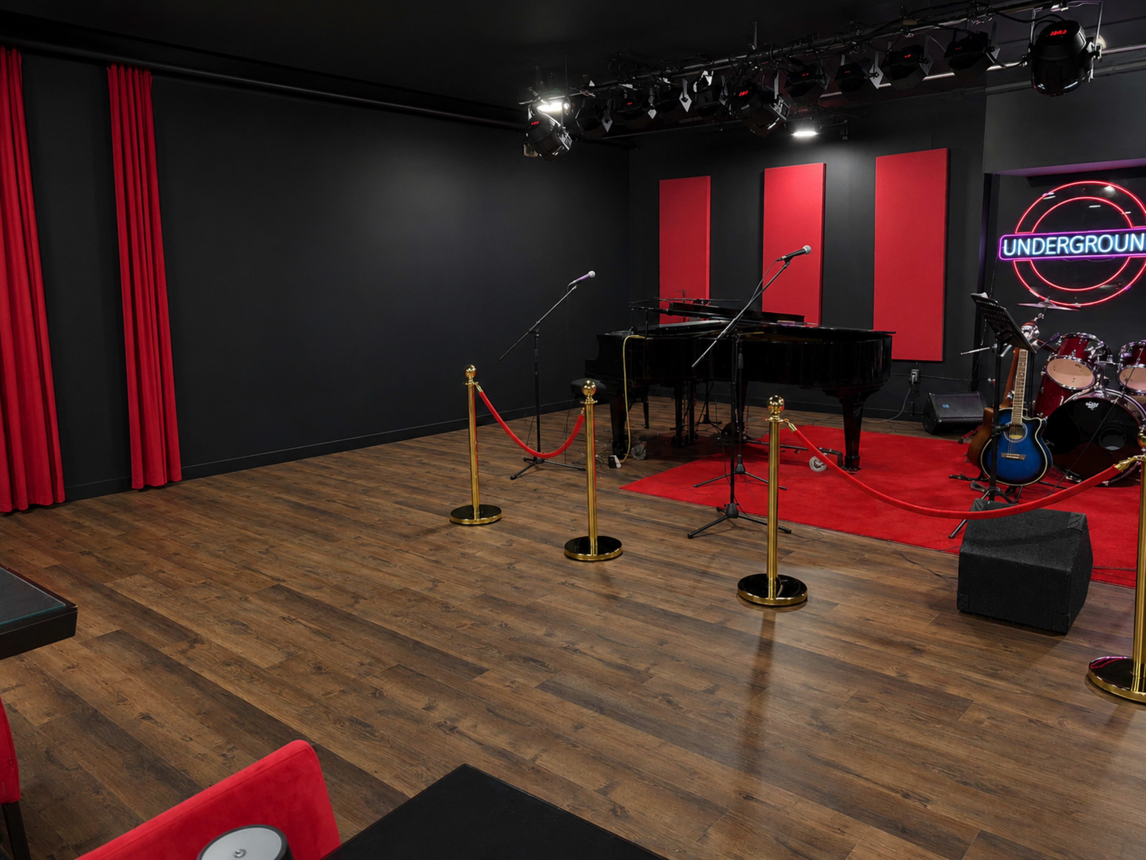 The image shows a music performance stage with a grand piano, drums, and microphones, surrounded by red curtains and a VIP rope barrier in a dimly lit room.