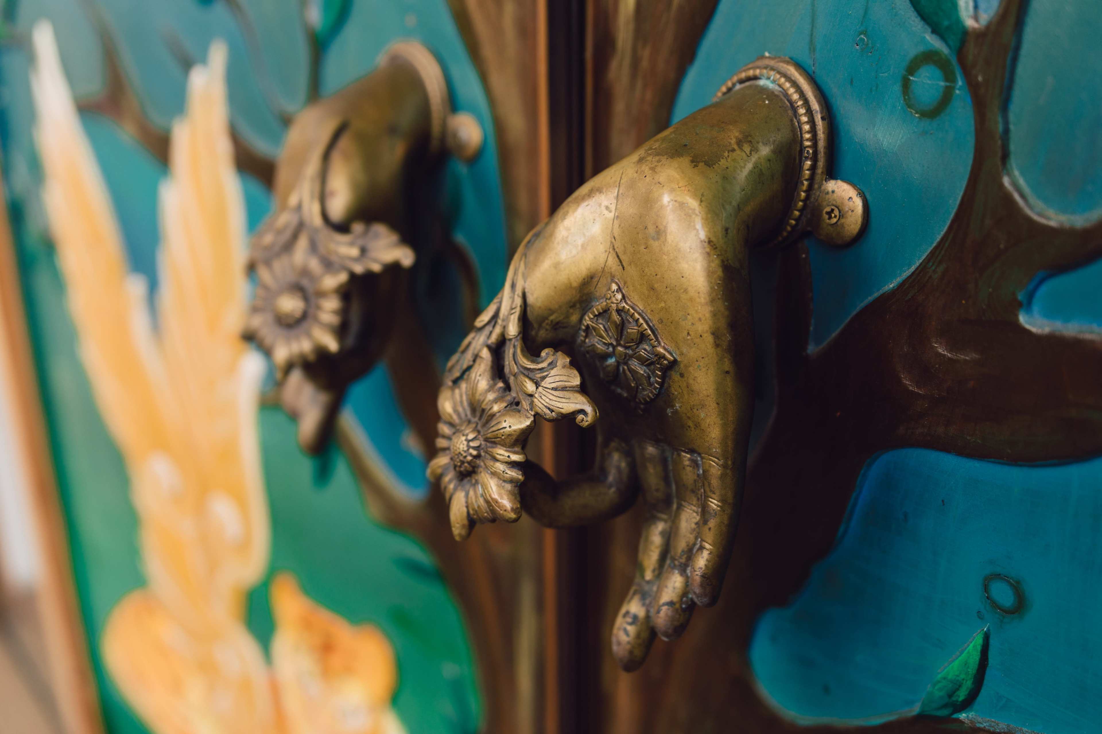 The image features two brass-handled doors adorned with intricate floral designs on a vibrant painted background.