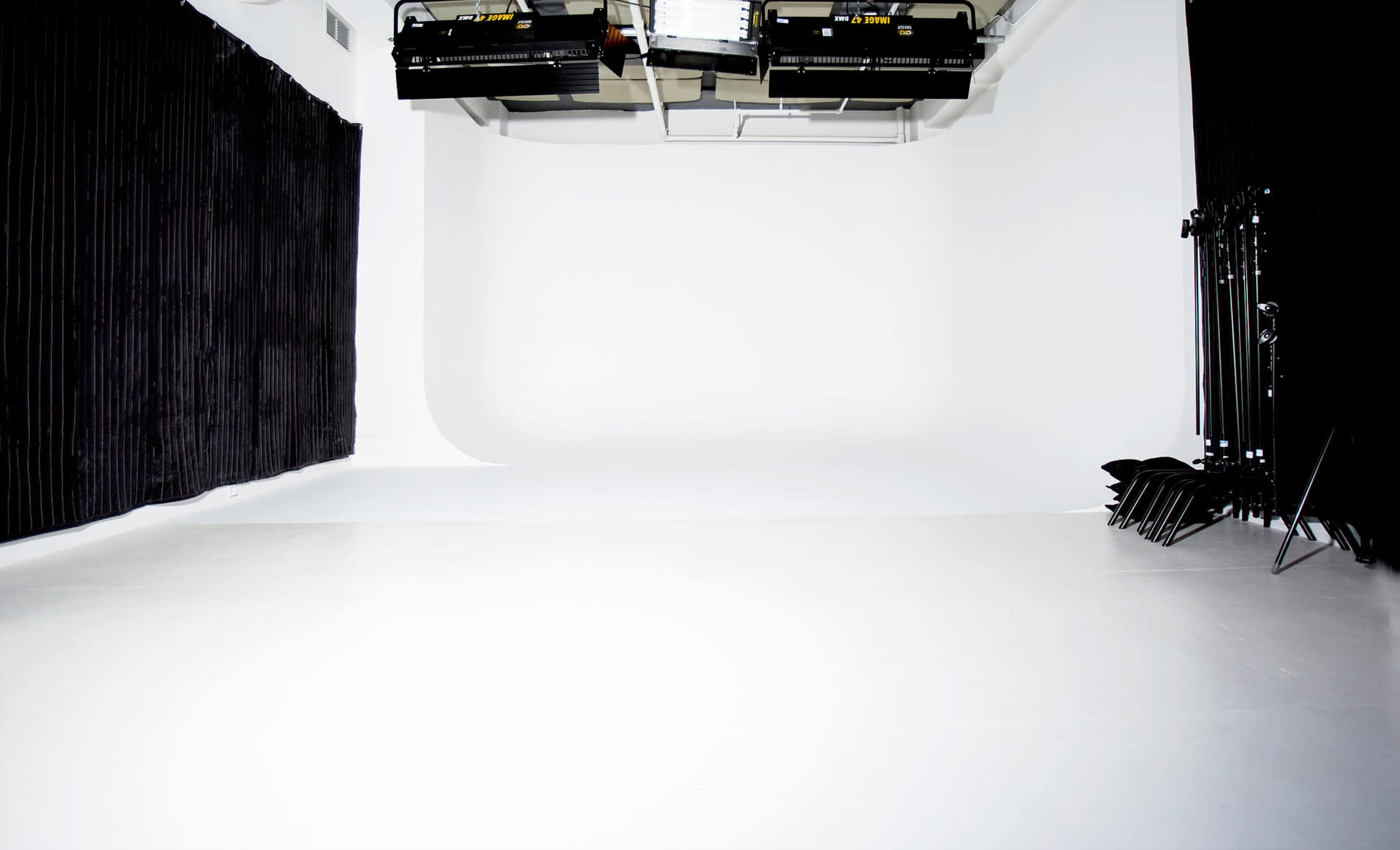 The image shows a spacious photography studio with black curtains on one side and white seamless backdrop.