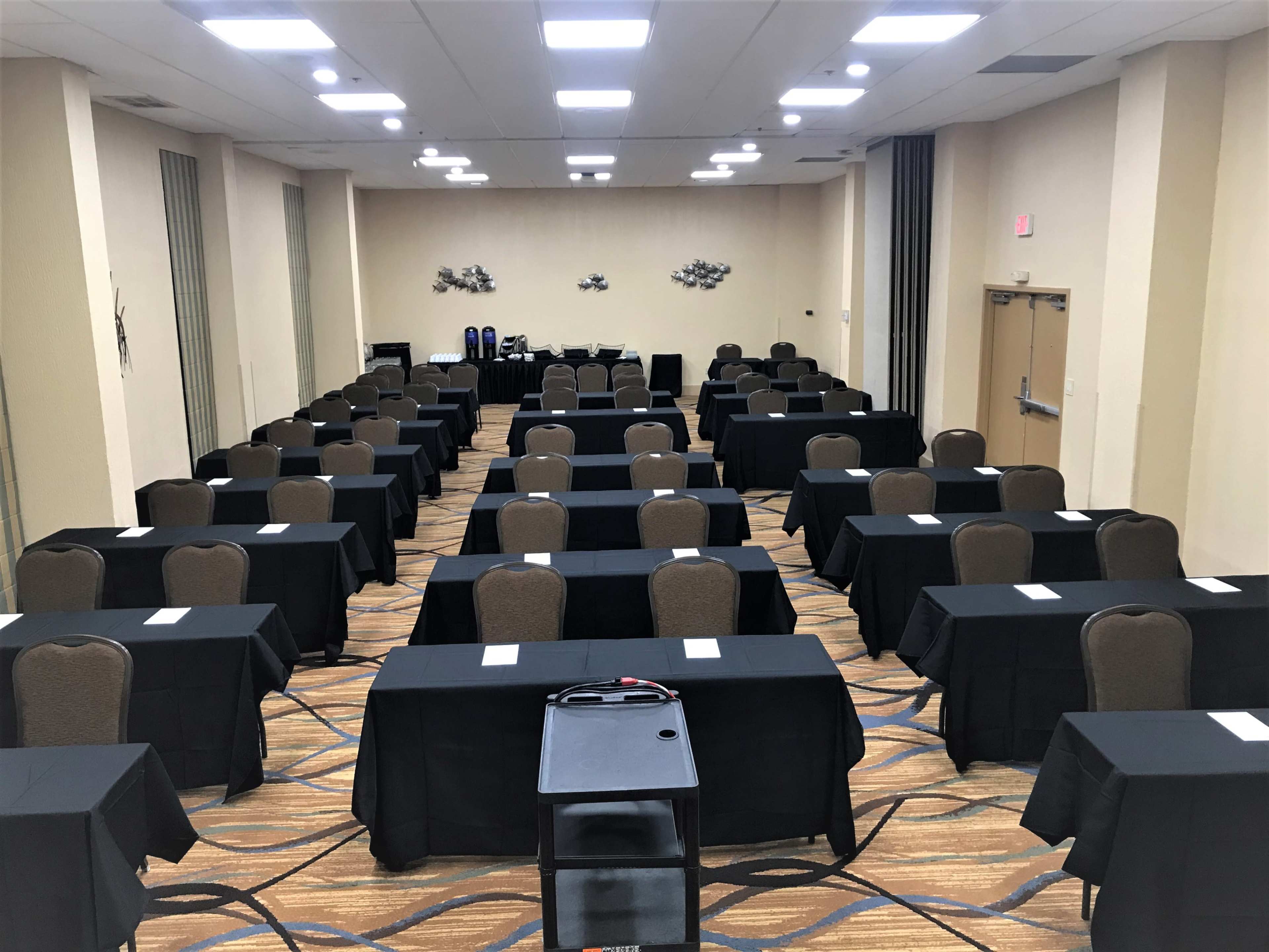 A conference room set up with rows of tables covered in black cloth and chairs arranged facing a central space.