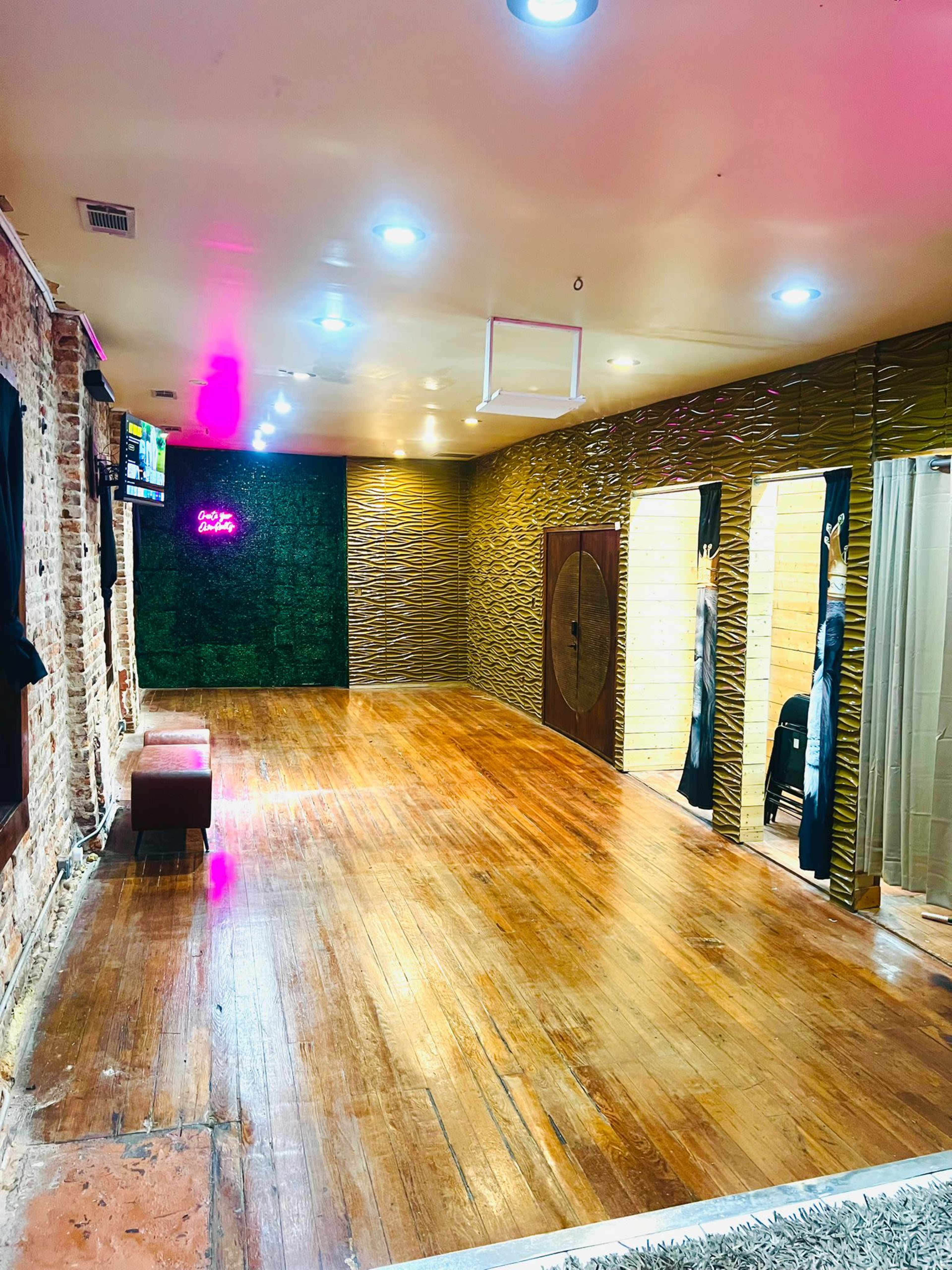 The image shows a spacious, well-lit interior room with wooden flooring, a green accent wall, and several changing areas with curtains.