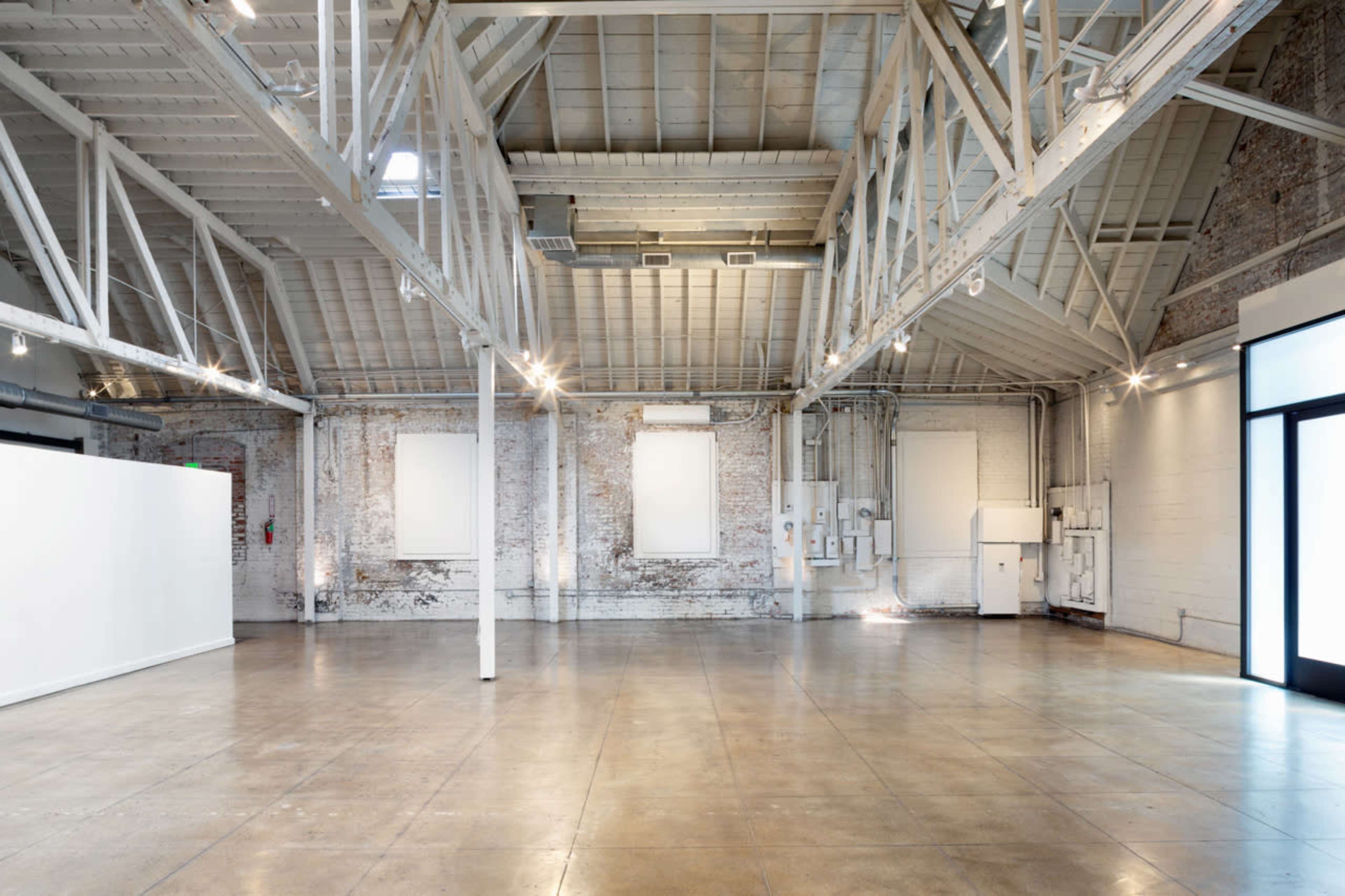 The image depicts a spacious, industrial-style interior with exposed brick walls, high ceilings, and polished concrete floors.