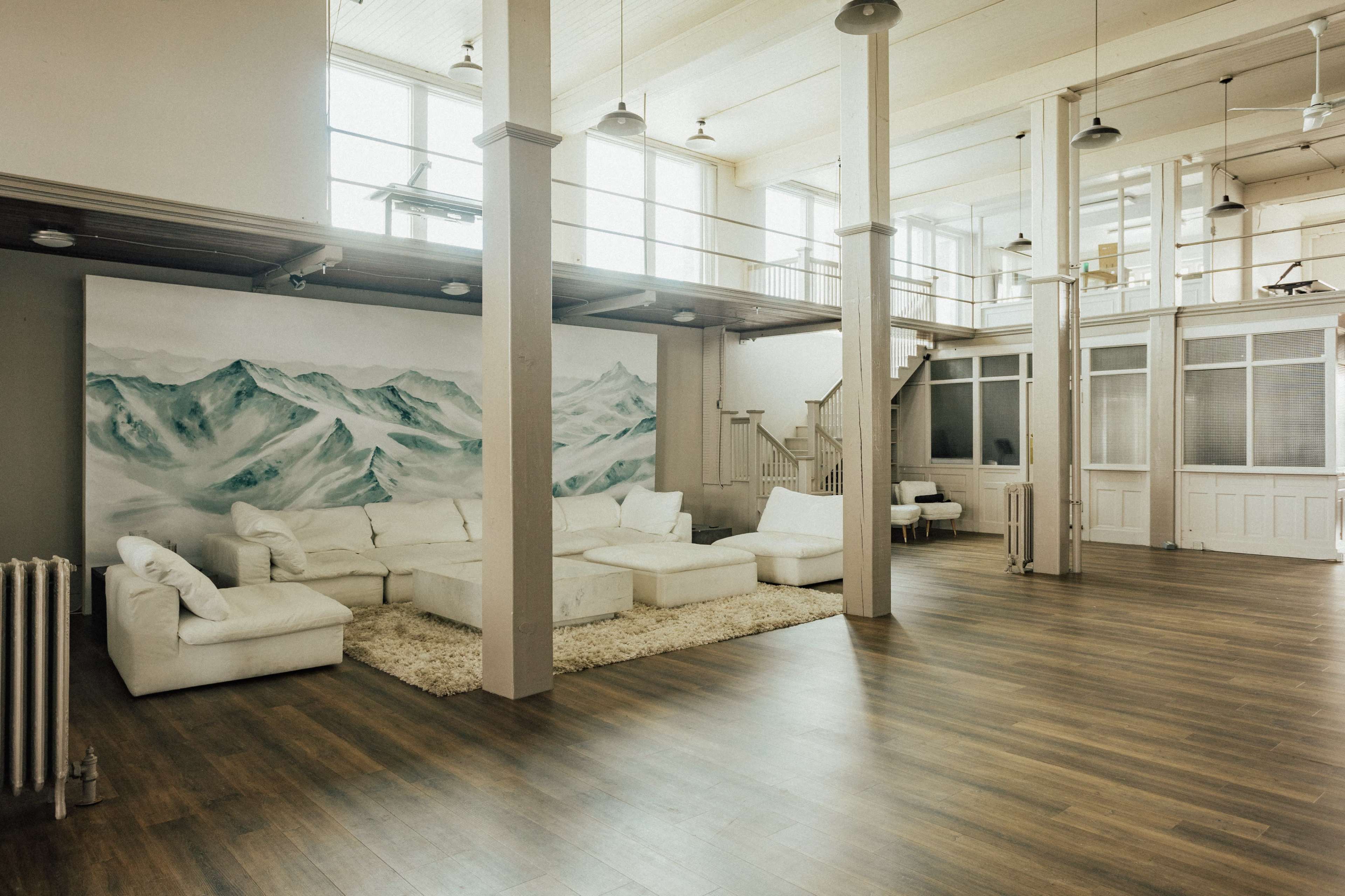 A spacious, modern interior with a white sectional sofa, a large area rug, and a mural of mountains on the wall.