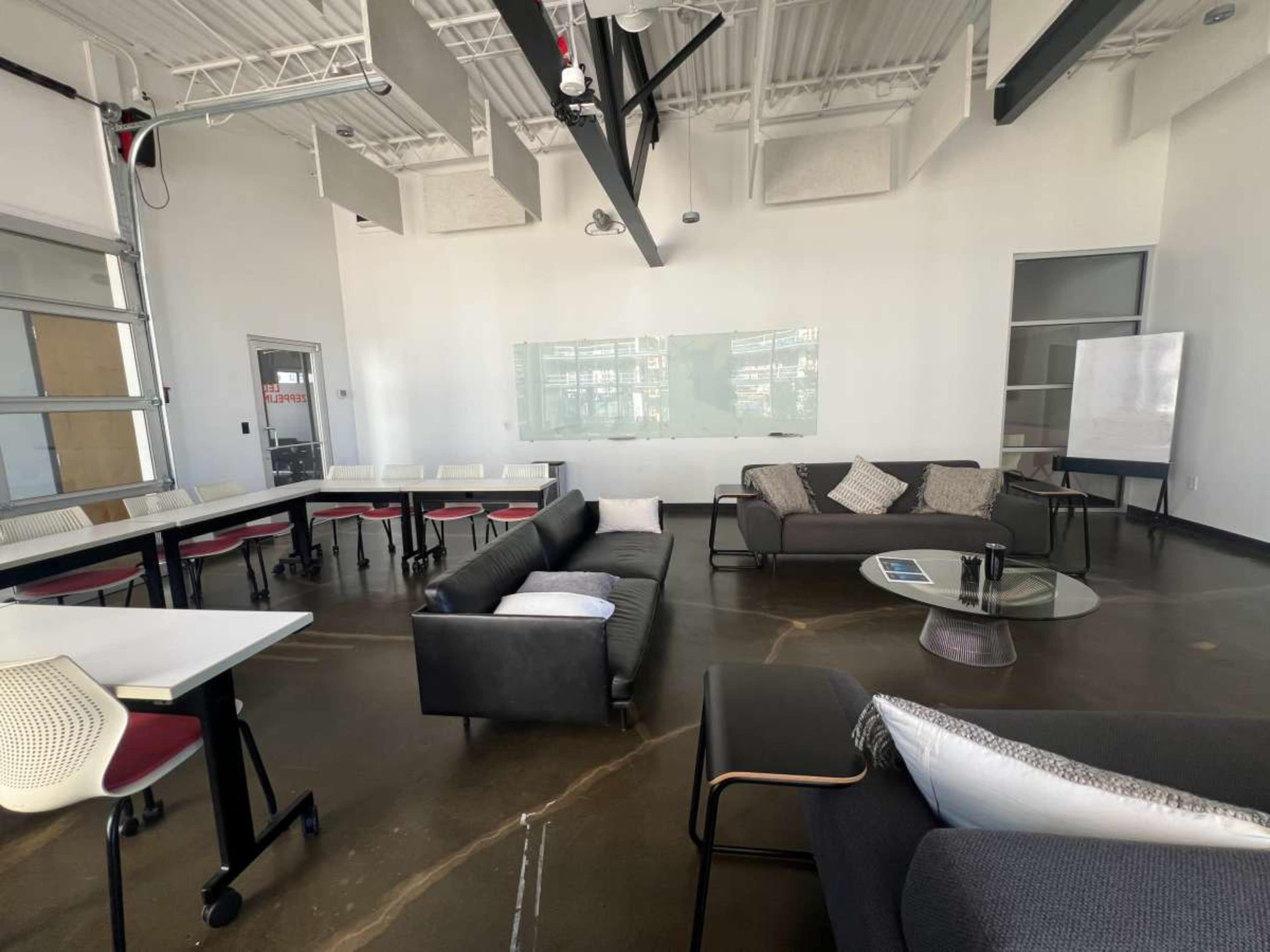 The image shows a modern, spacious meeting room with a variety of seating options, including couches and chairs arranged around a central coffee table.