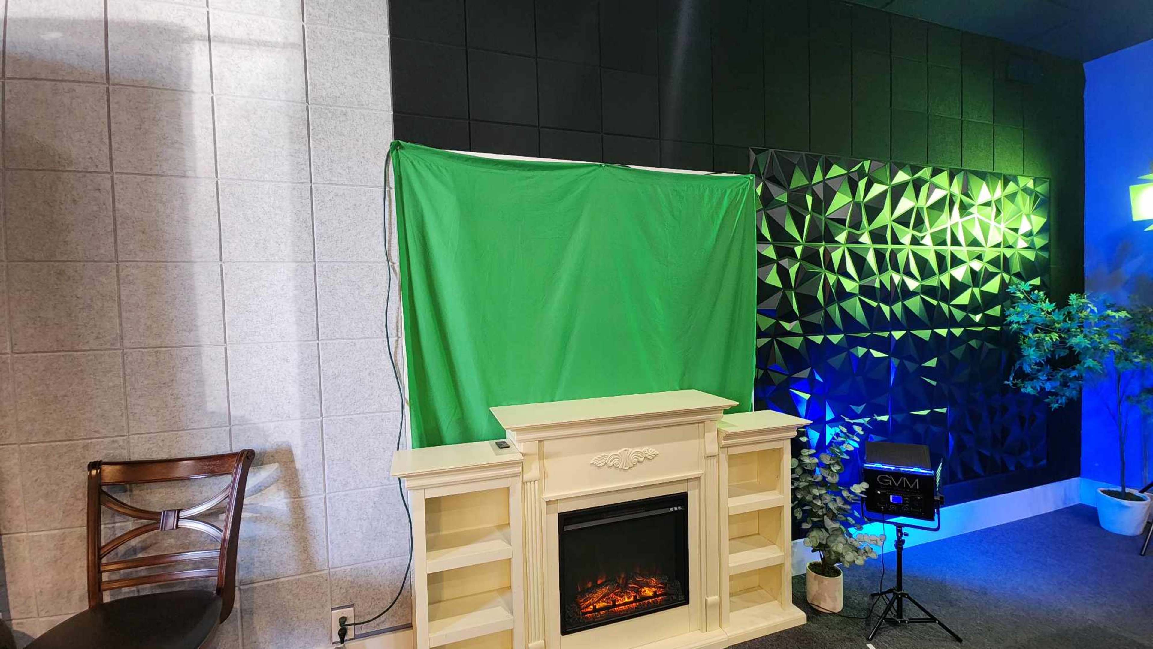 A green screen is set up in front of a decorative fireplace, flanked by textured black and gray walls with ambient lighting.