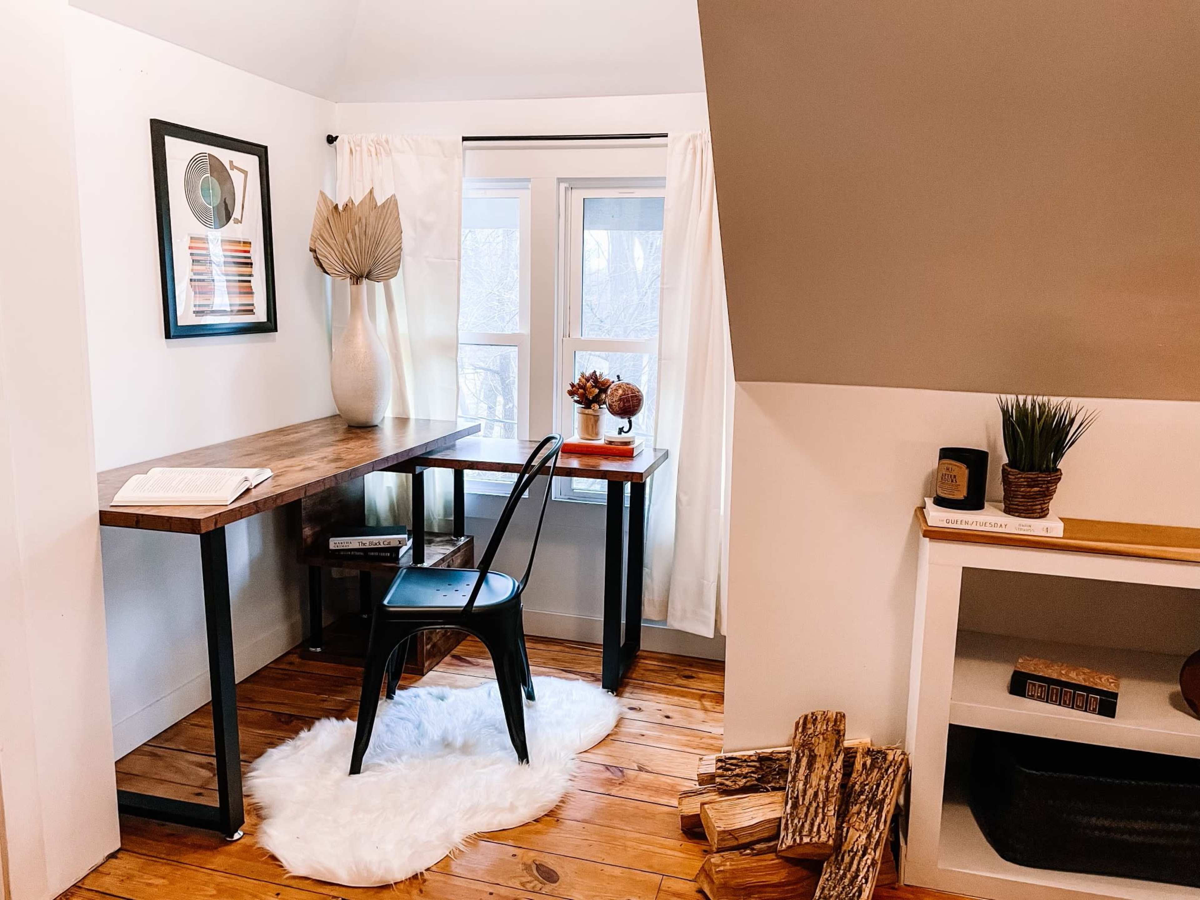 A small workspace featuring a wooden desk, a black chair, a decorative vase, and a window with natural light.