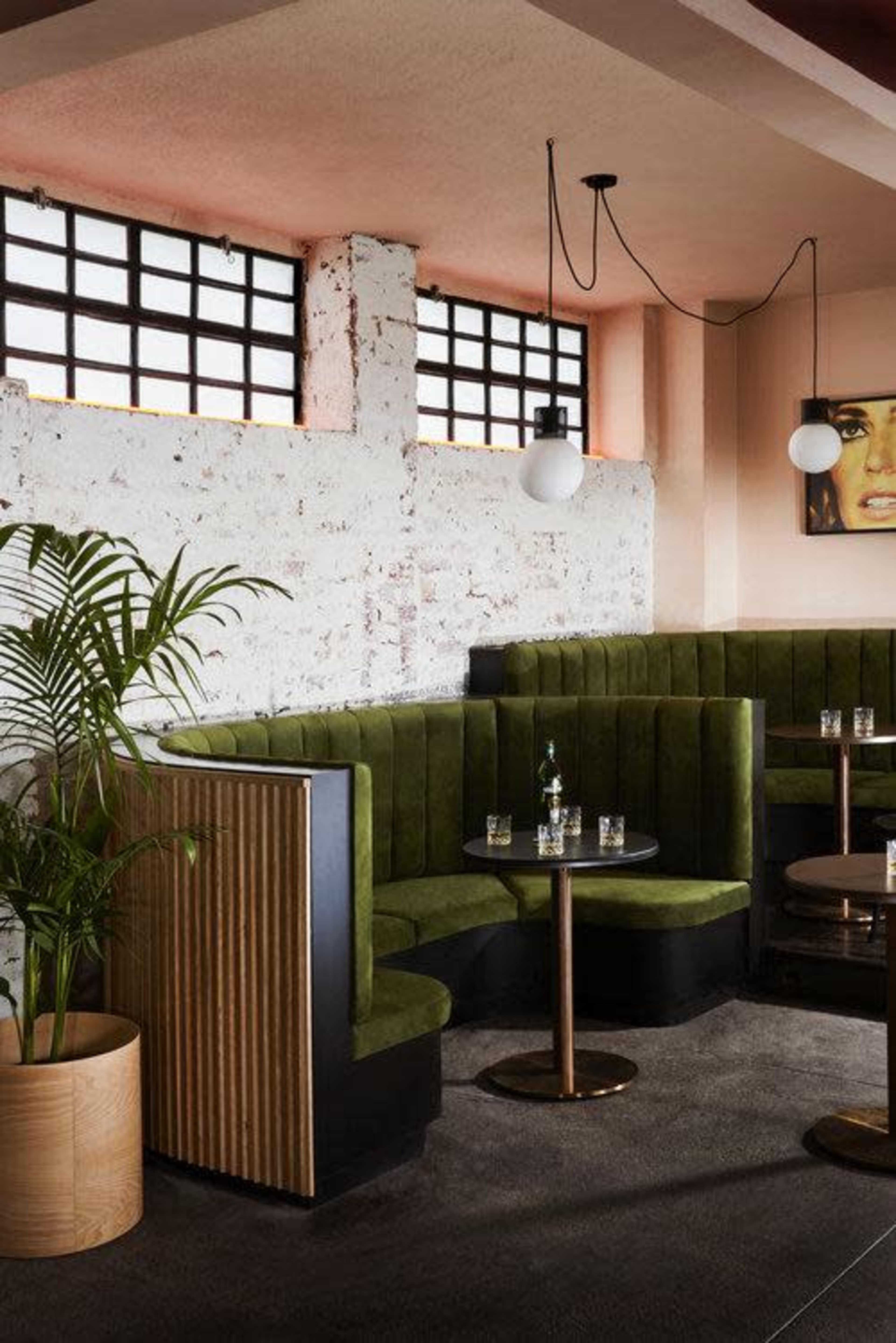 A modern lounge area with green upholstered seating, a round table, and large windows allowing natural light to enter.