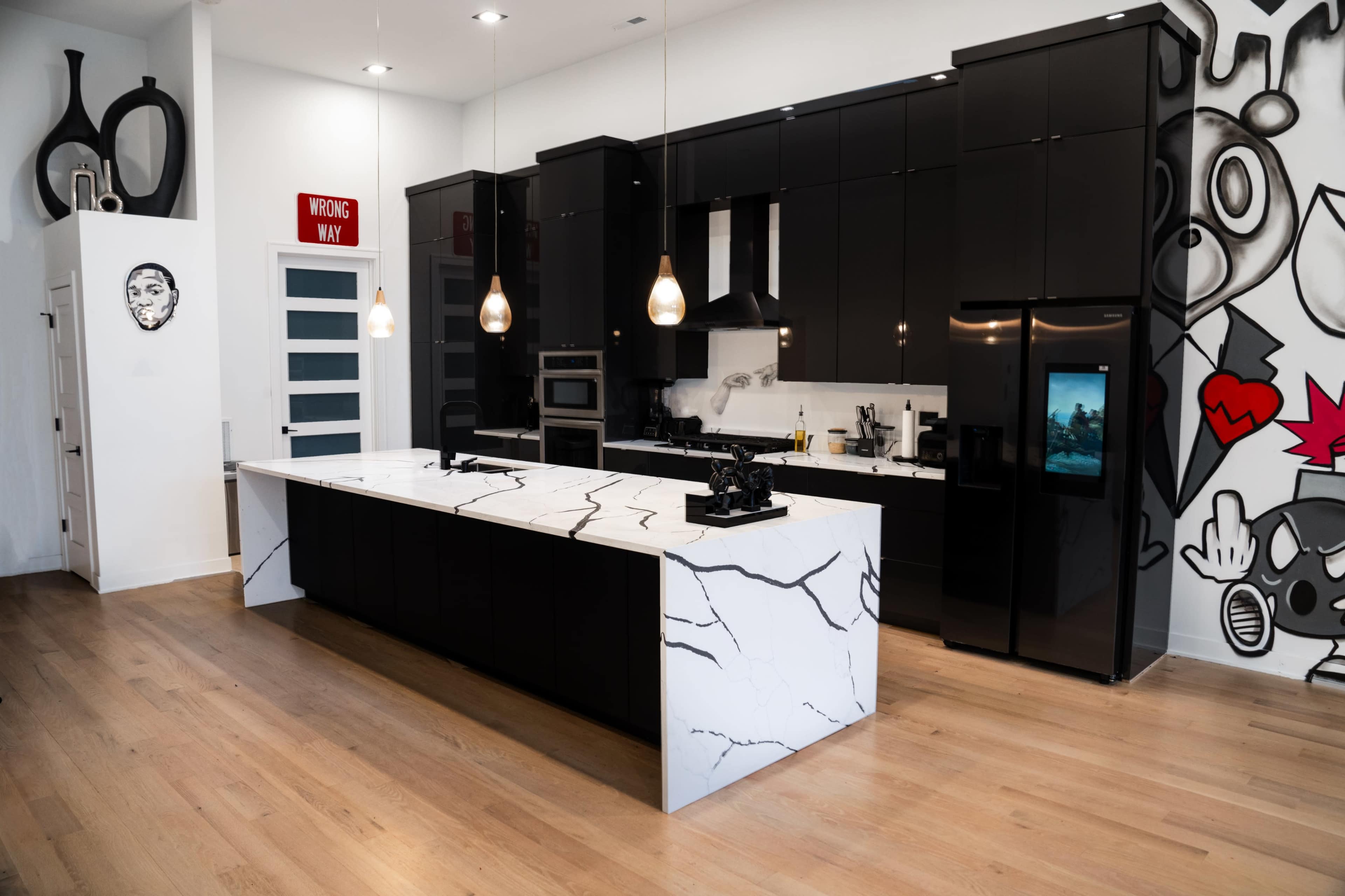 A modern kitchen with black cabinetry, a large marble island, and a wall featuring colorful graffiti art.
