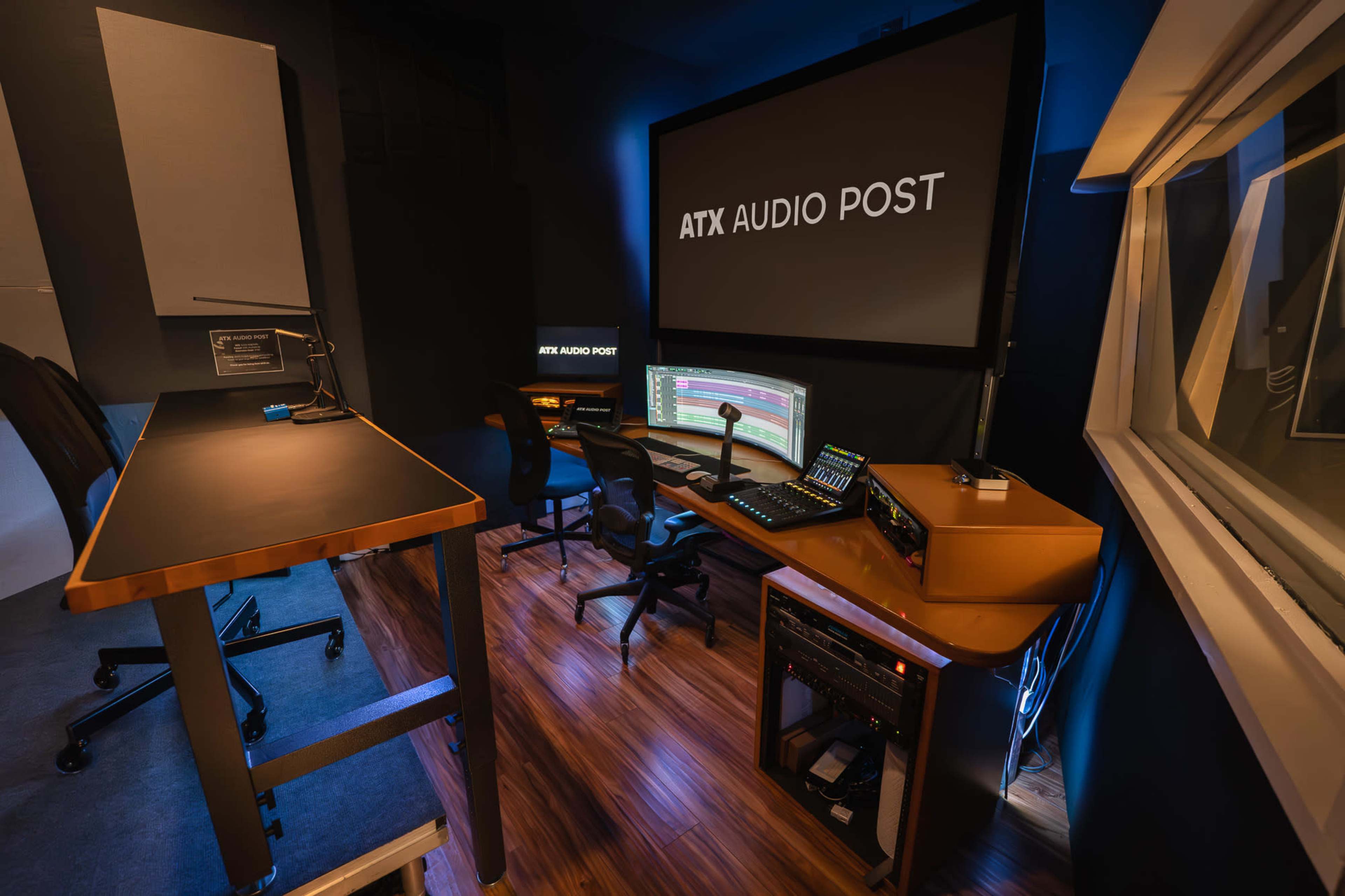The image shows a modern audio post-production studio featuring a large monitor, editing workstation, and various audio equipment set against a dark, acoustically treated environment.