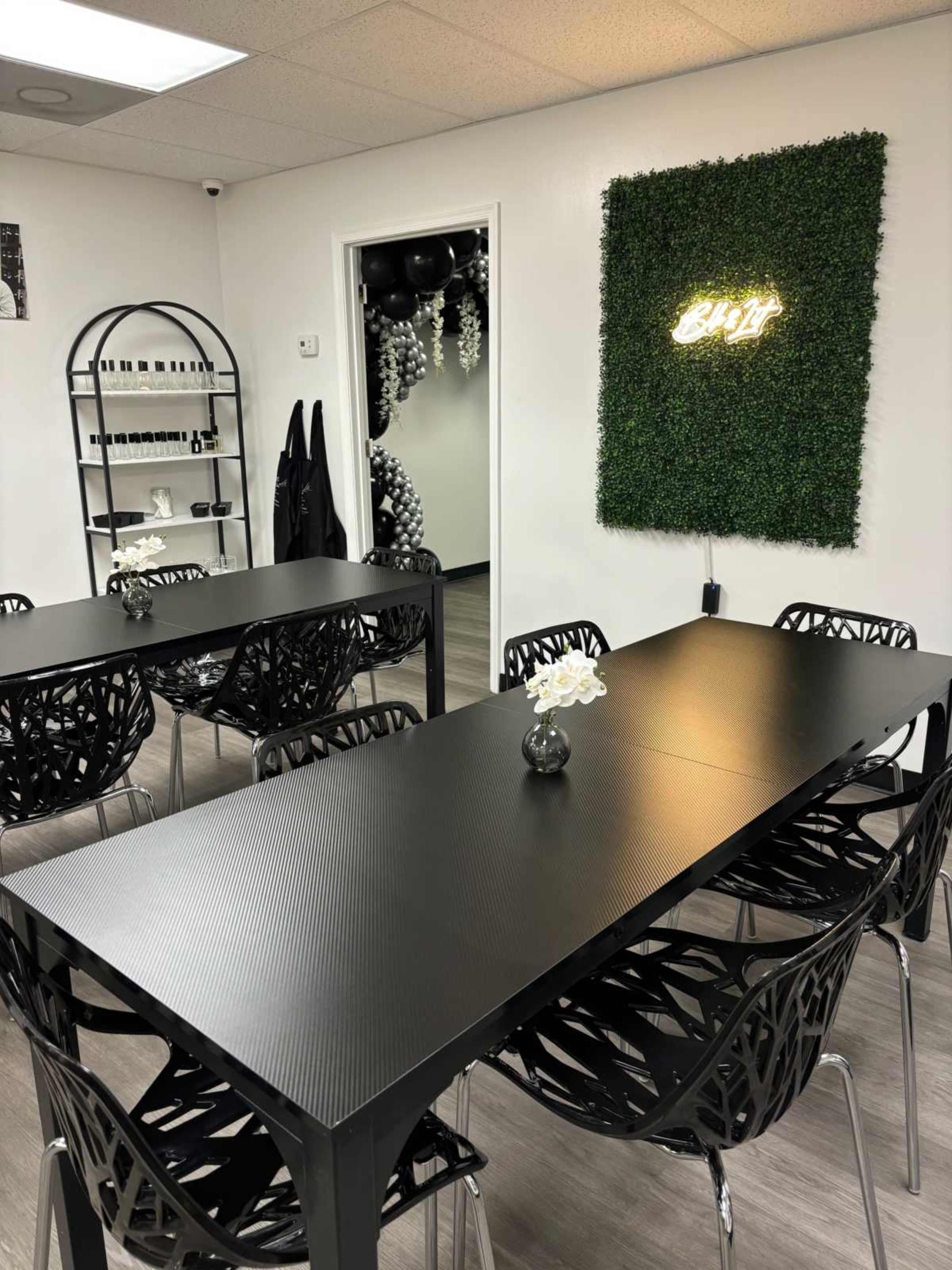 The image shows a modern meeting room with black tables, black chairs, and a decorative green wall featuring a neon sign.