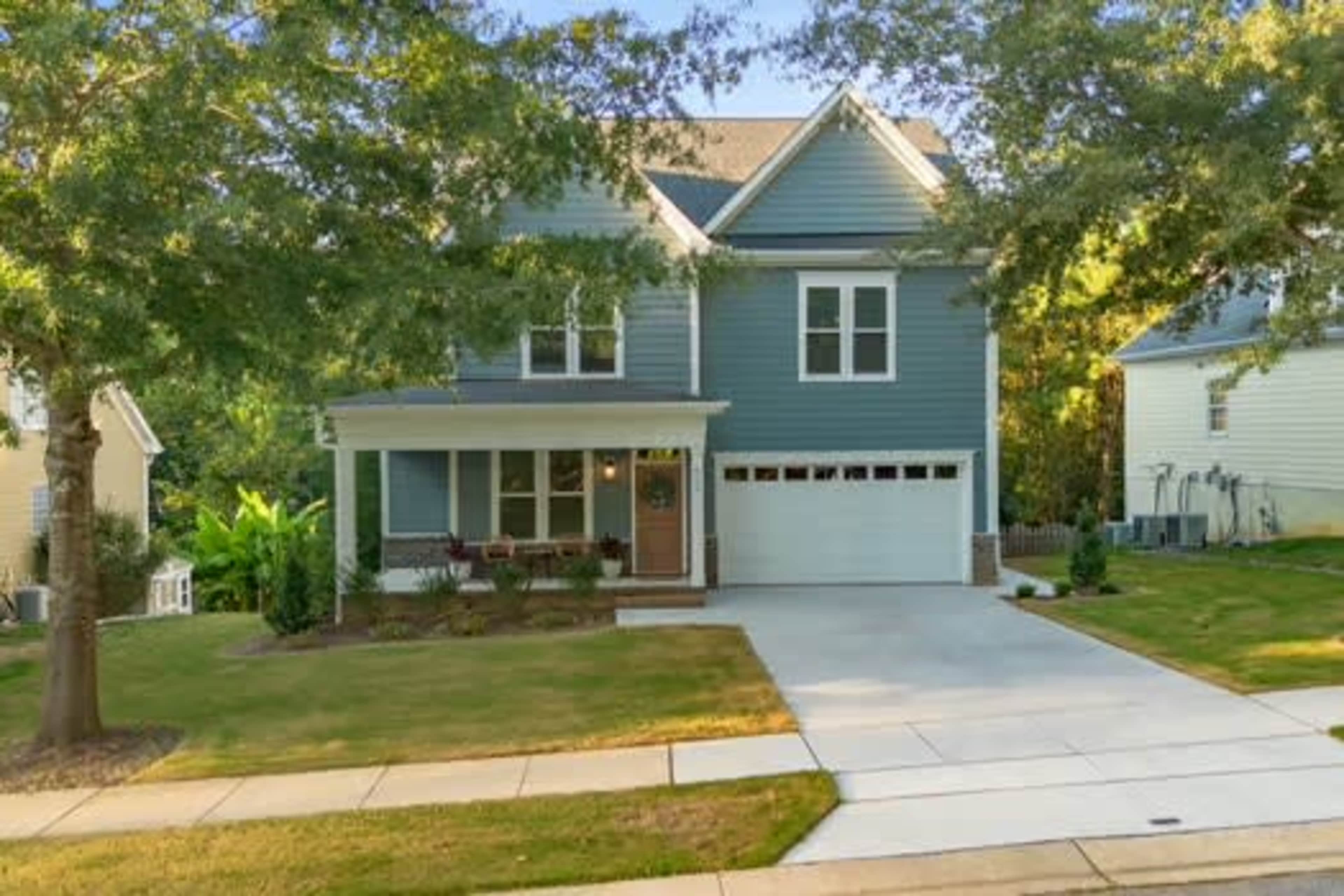 The image shows a two-story blue house with a front porch and a two-car garage, situated on a landscaped lawn in a residential neighborhood.