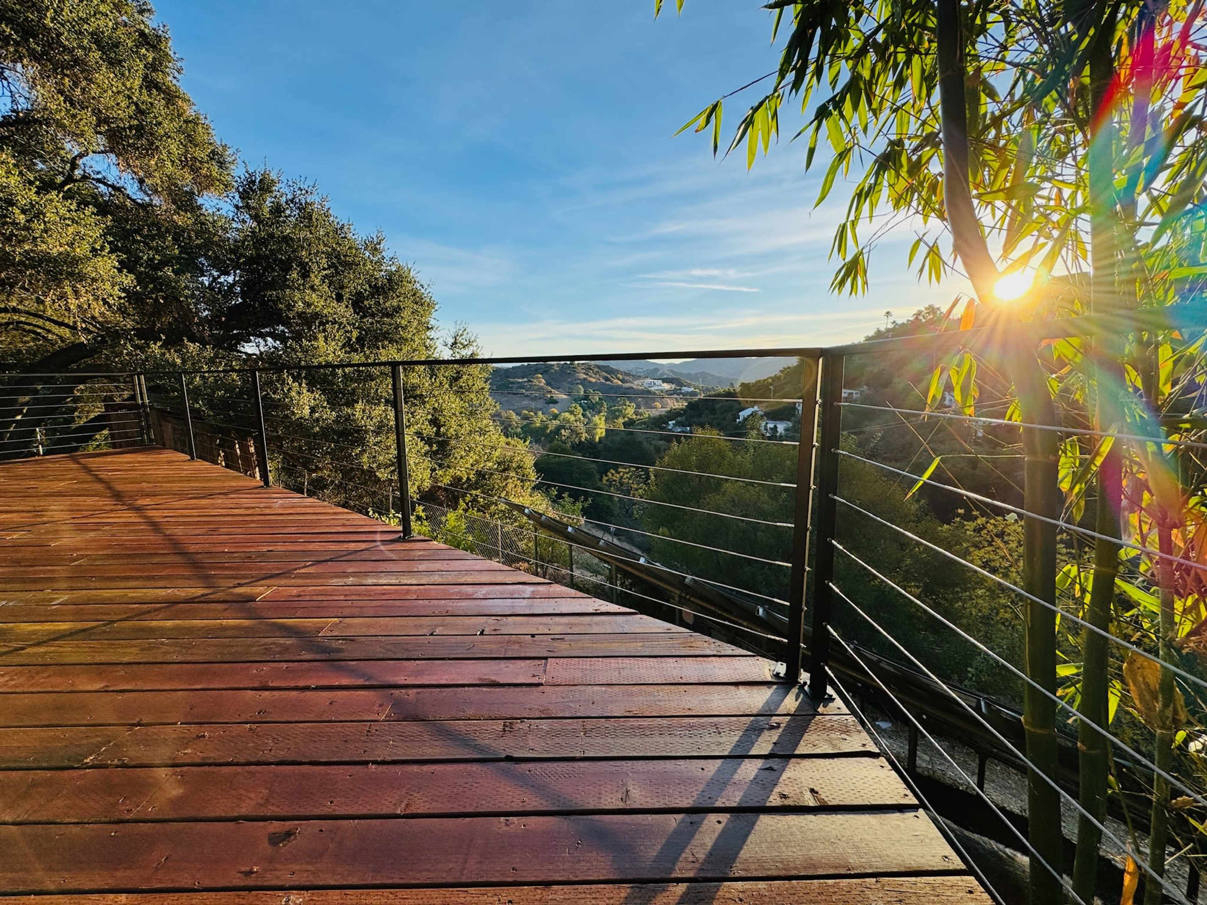 A wooden deck overlooks hills and trees bathed in the light of a setting sun.