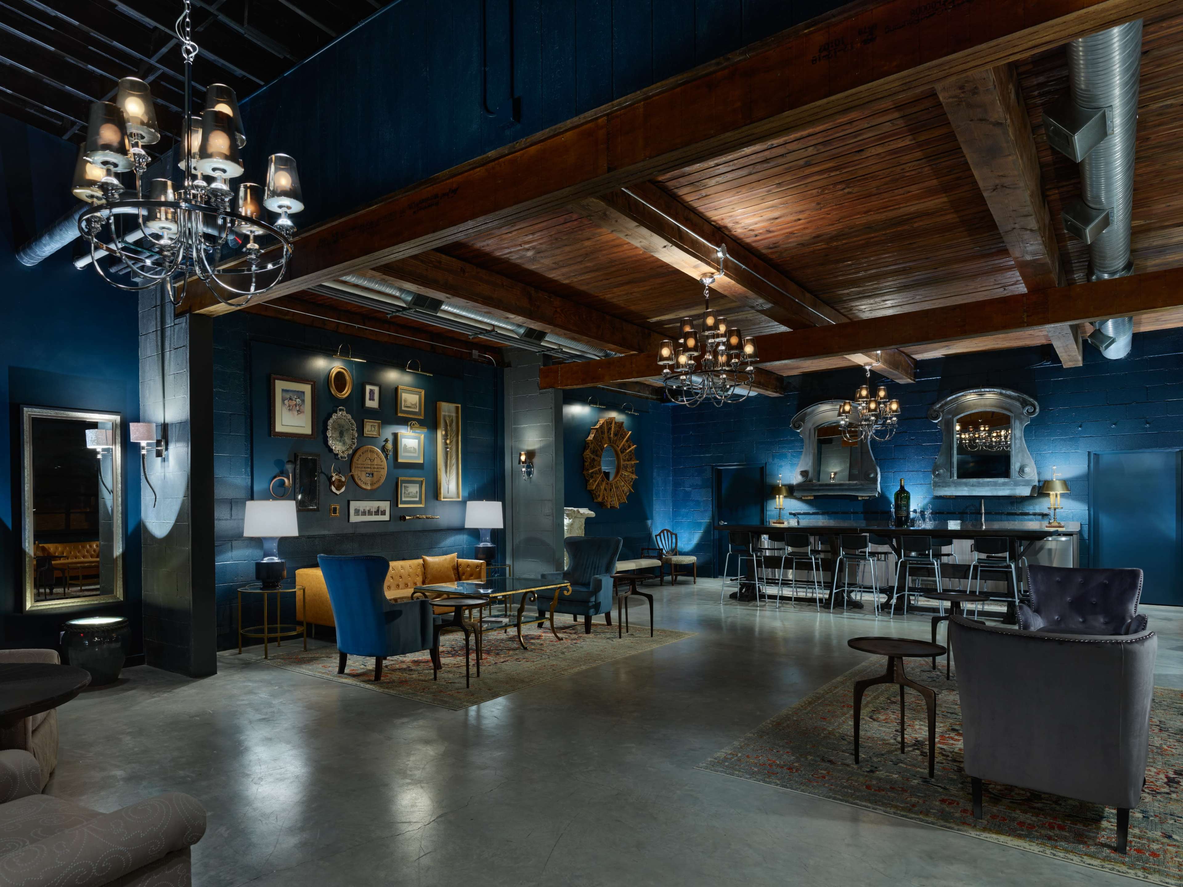 The image shows a spacious, stylish lounge area with dark blue walls, wooden beams, and various seating arrangements centered around decorative lighting fixtures.
