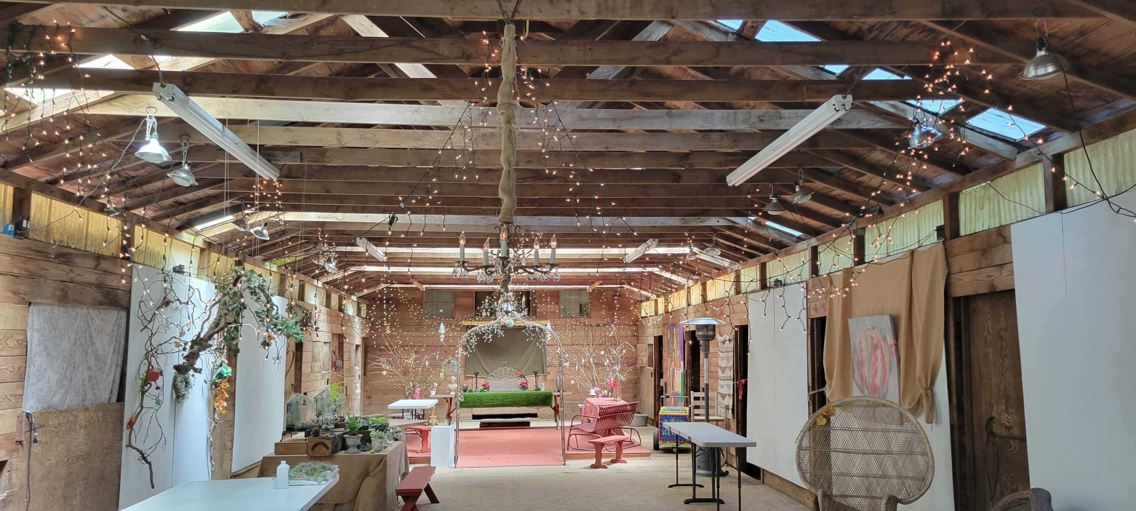An indoor space with wooden beams, string lights, and various seating areas, including pink chairs and a green couch.