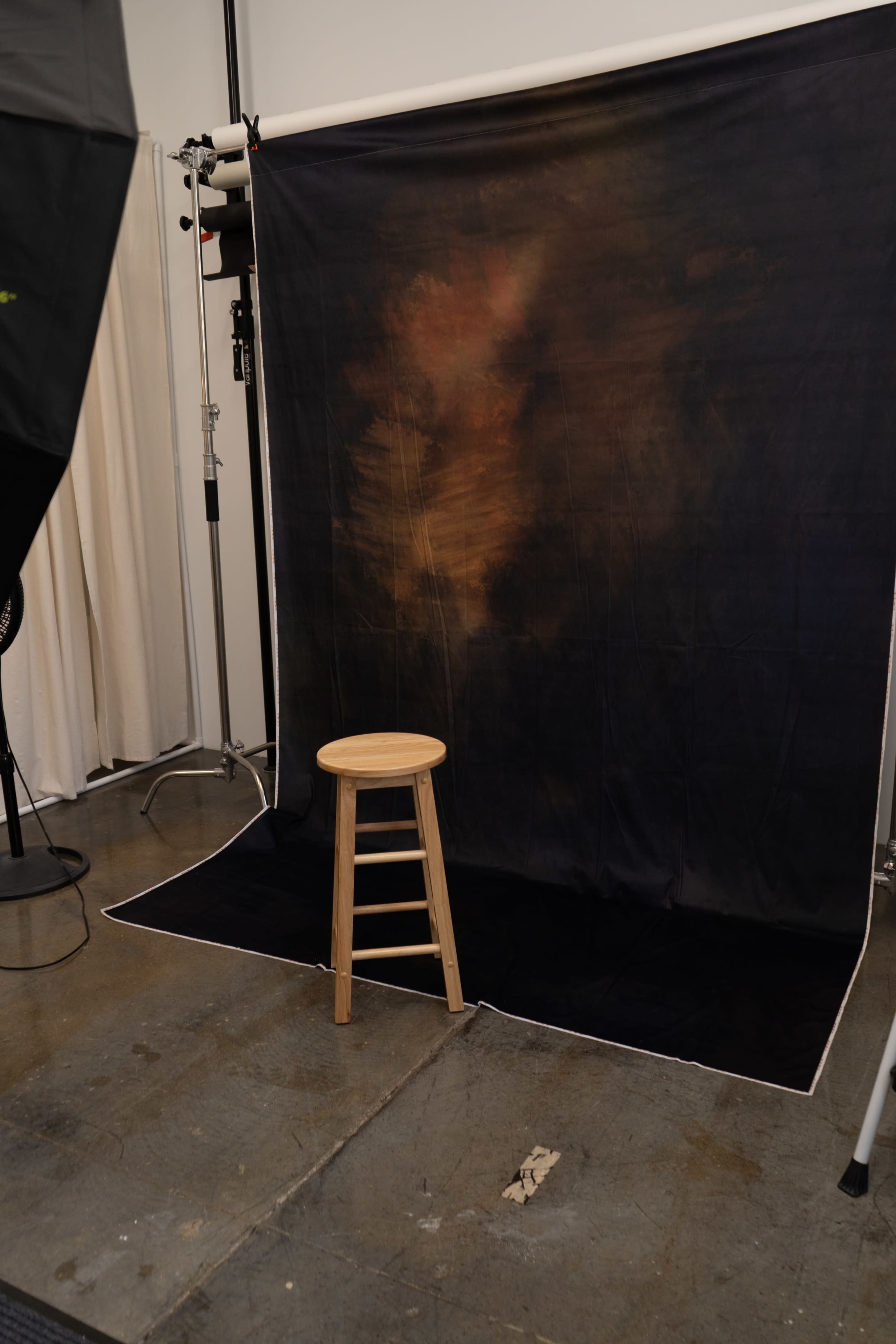 The image shows a photography studio setup with a wooden stool placed in front of a dark, textured backdrop.