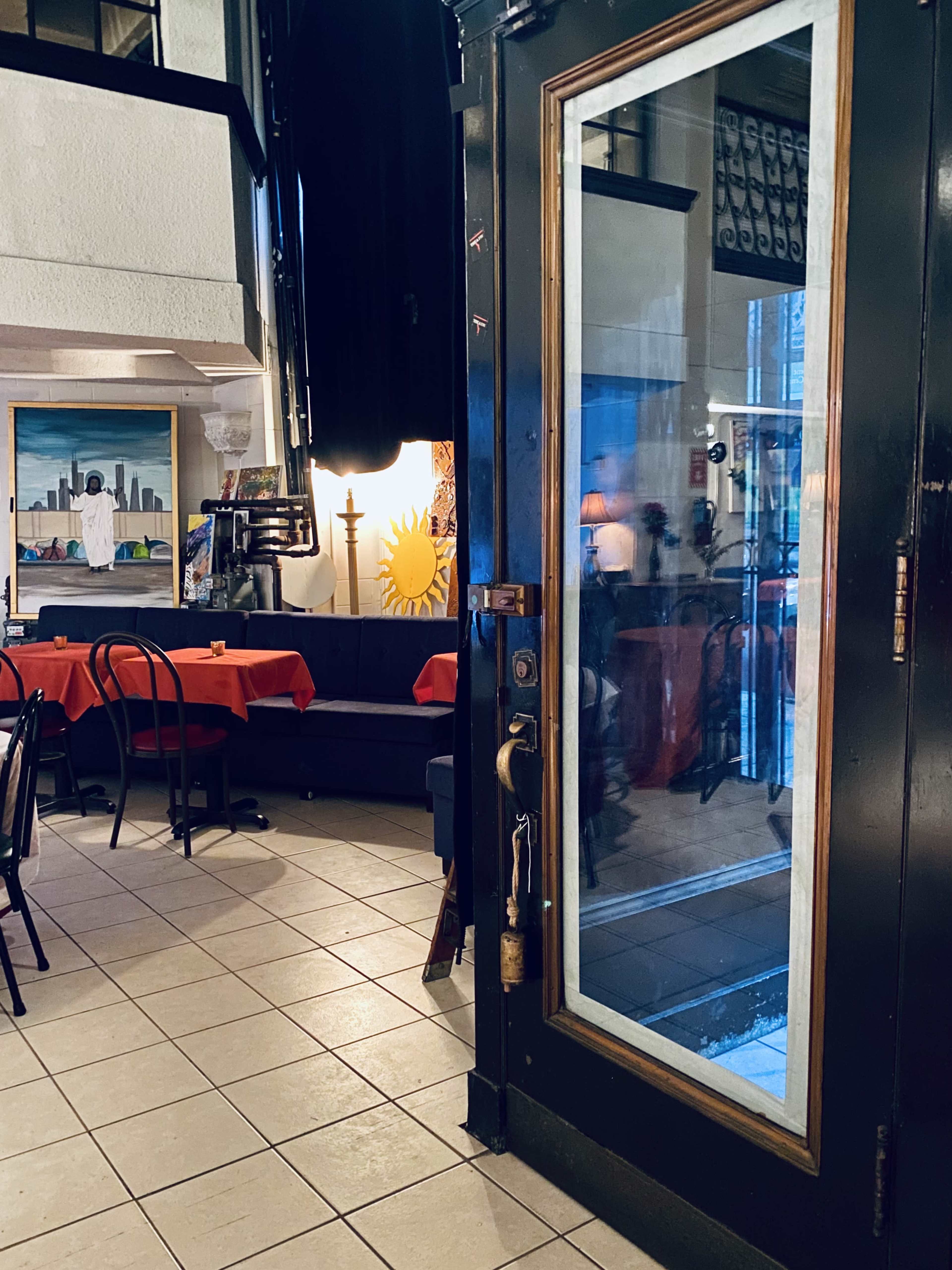 A partially open glass door leading into a restaurant with red-tableclothed tables and artwork on the walls.