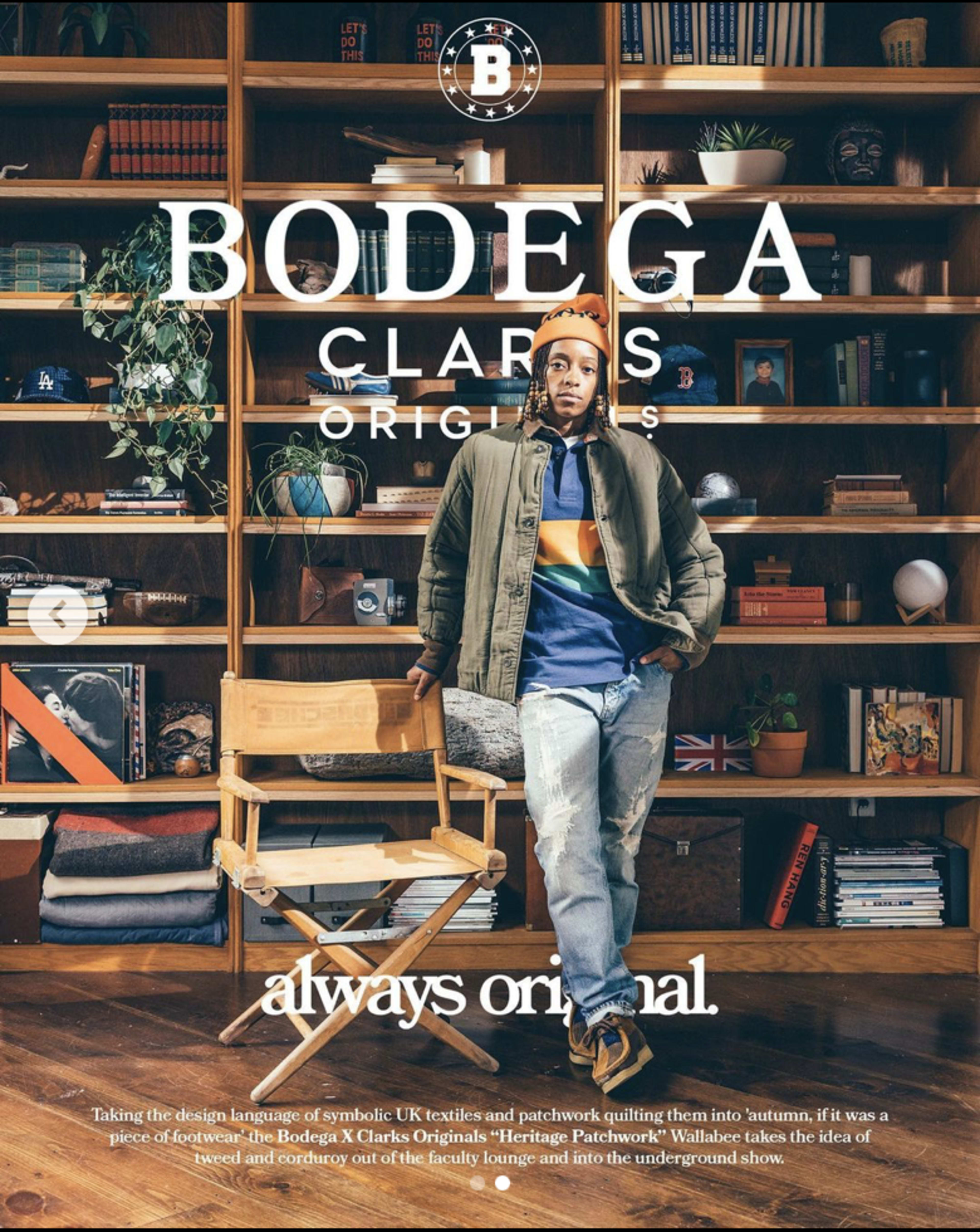 A person stands in front of a wooden shelving unit filled with various books and decorative items, wearing a colorful jacket and a beanie.