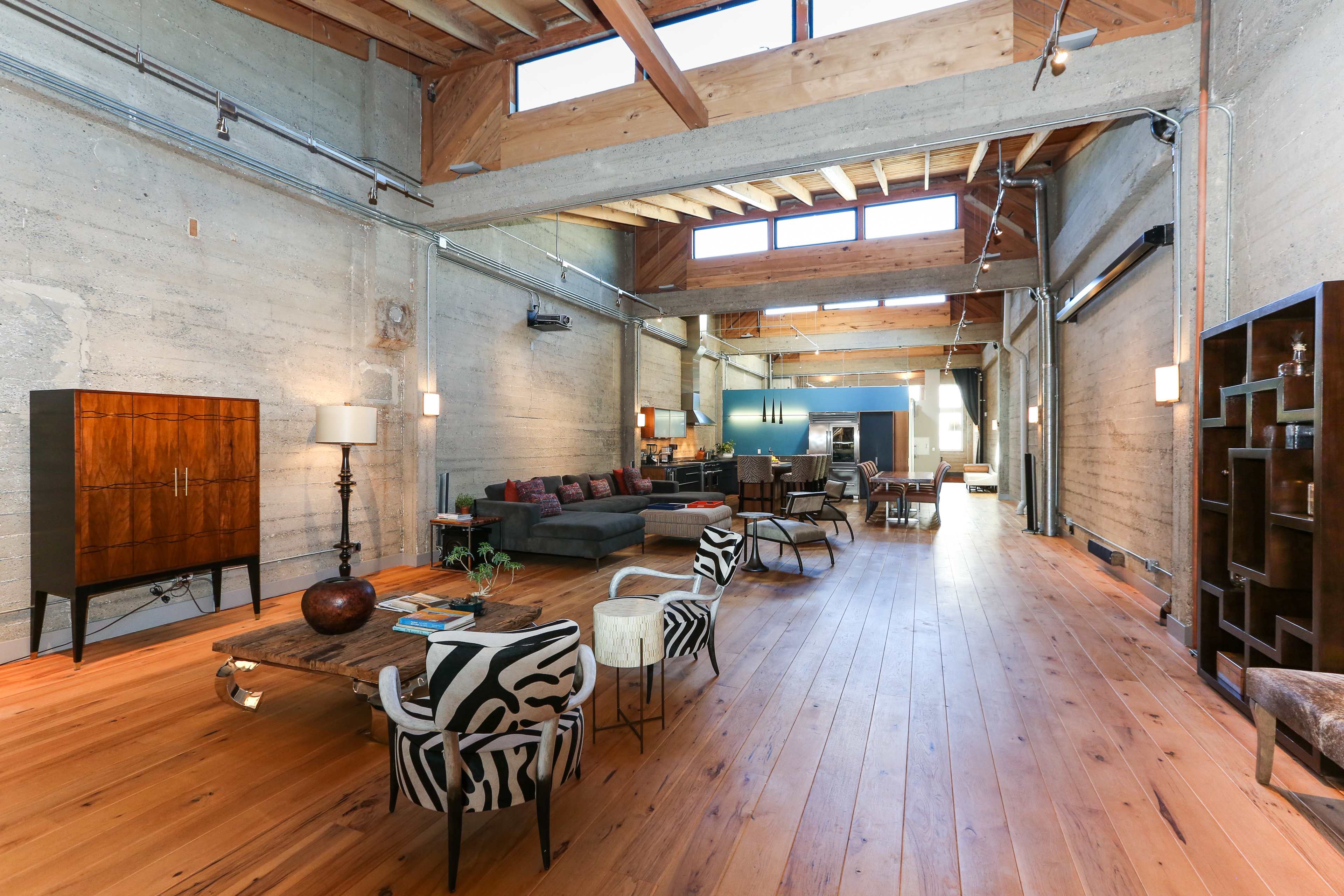 A spacious, modern loft with wooden beams, large windows, and an open layout featuring a living area, dining space, and kitchen.